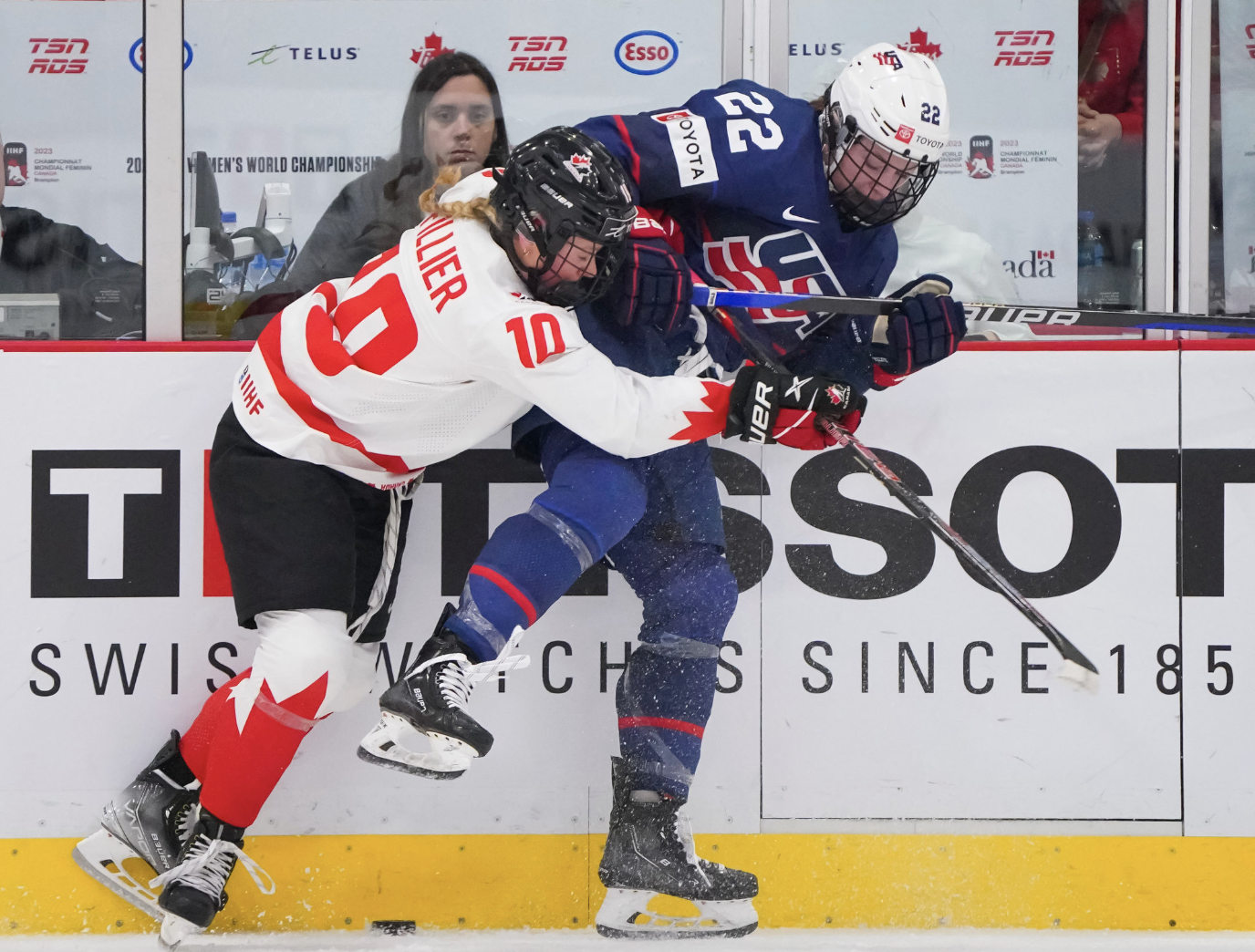 Fillier (left in white) hits Janecke (right in navy) along the boards. Fillier is more hunched over than Janceke, whose right leg is in the air. The puck is in between them.