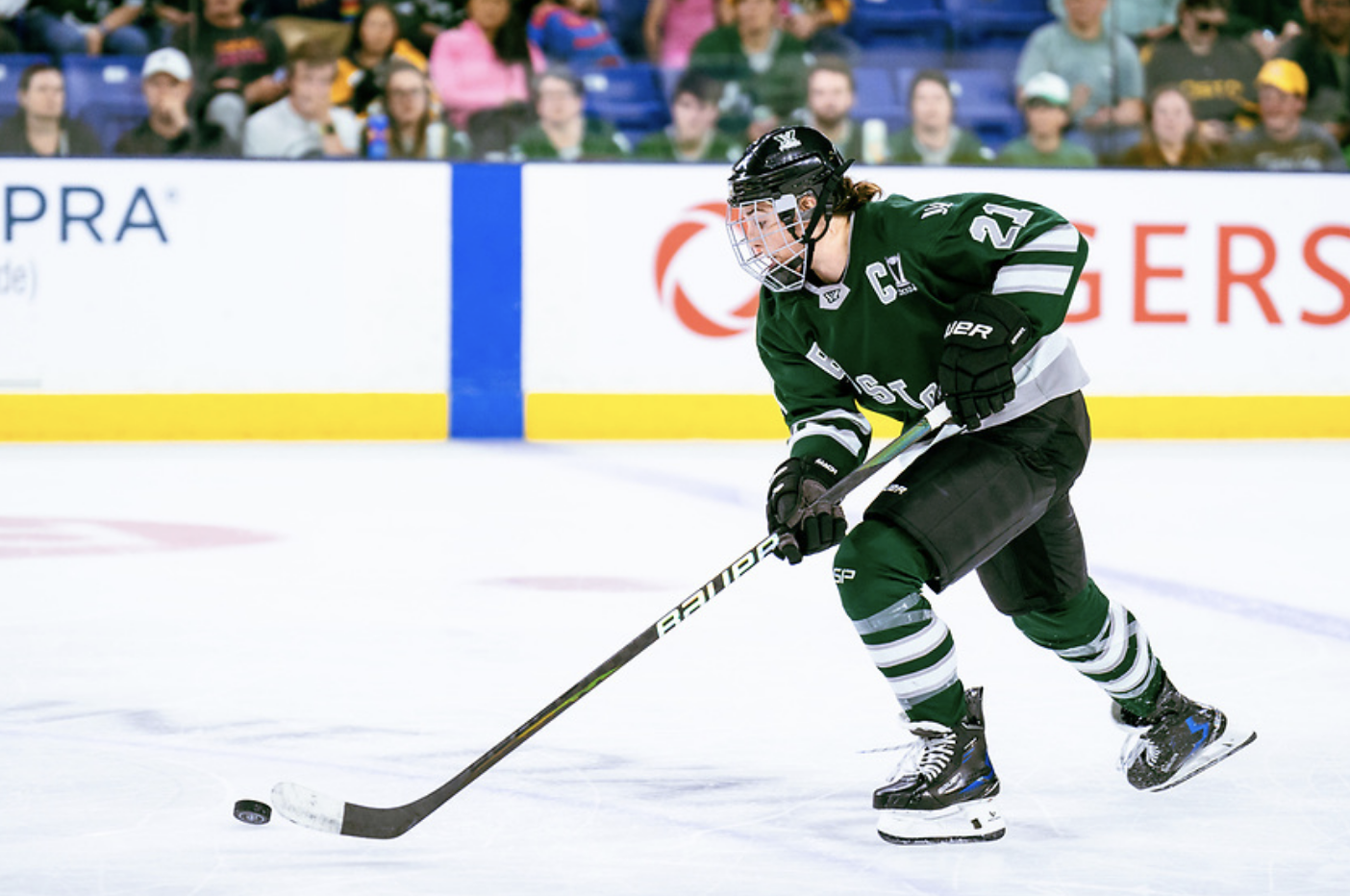 Knight skates up ice with the puck. She is mid-stick handle, and wearing a green home uniform.
