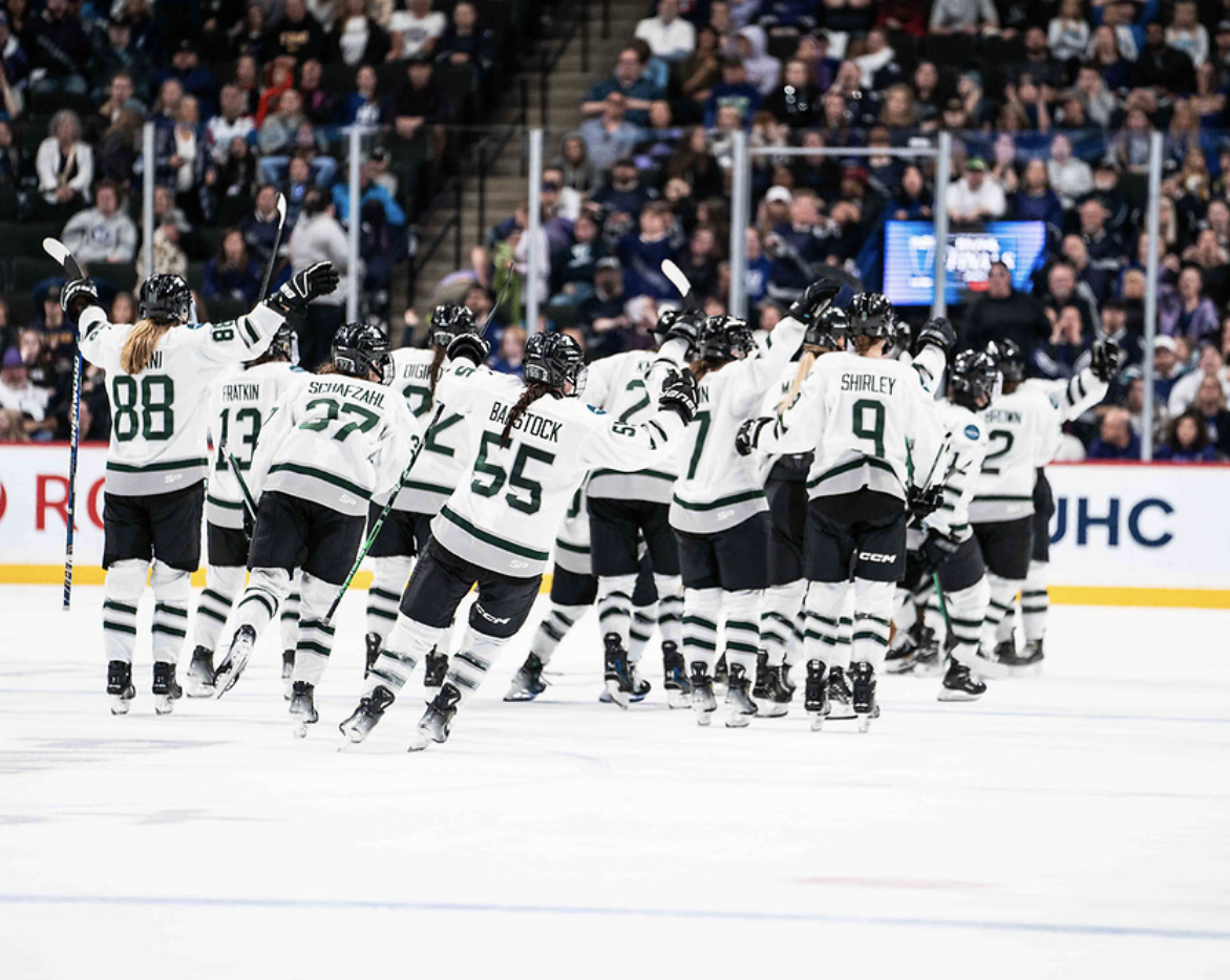 PWHL Boston skates off the ice while celebrating their Game 4 win in the PWHL Finals. Most of them are raising their arms. They're all back-to the camera wearing white away uniforms.
