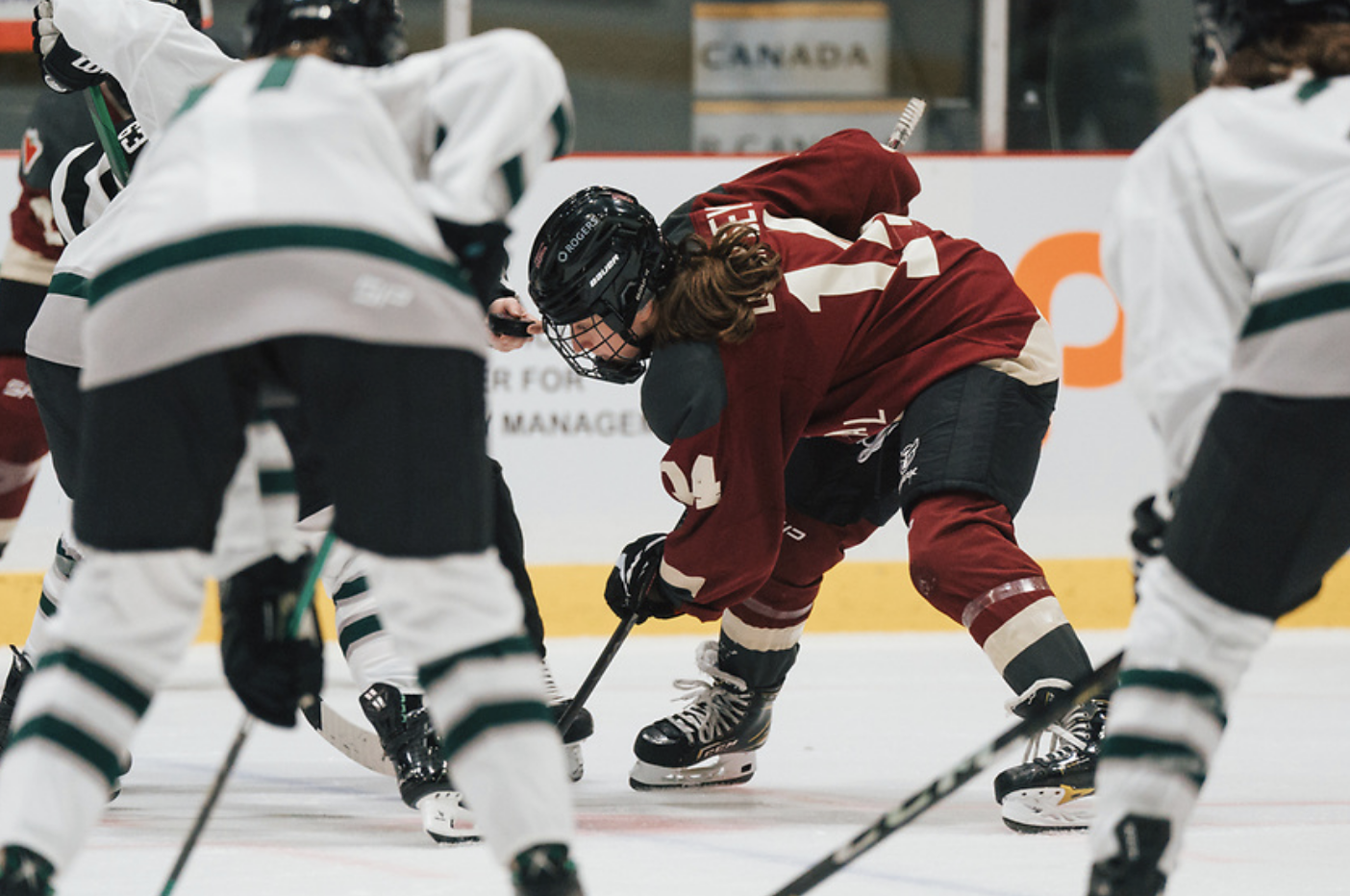 Dempsey is bent over with her stick in the face-off circle, look at the puck in the referee's hand. She is wearing a maroon Montrรฉal jersey.