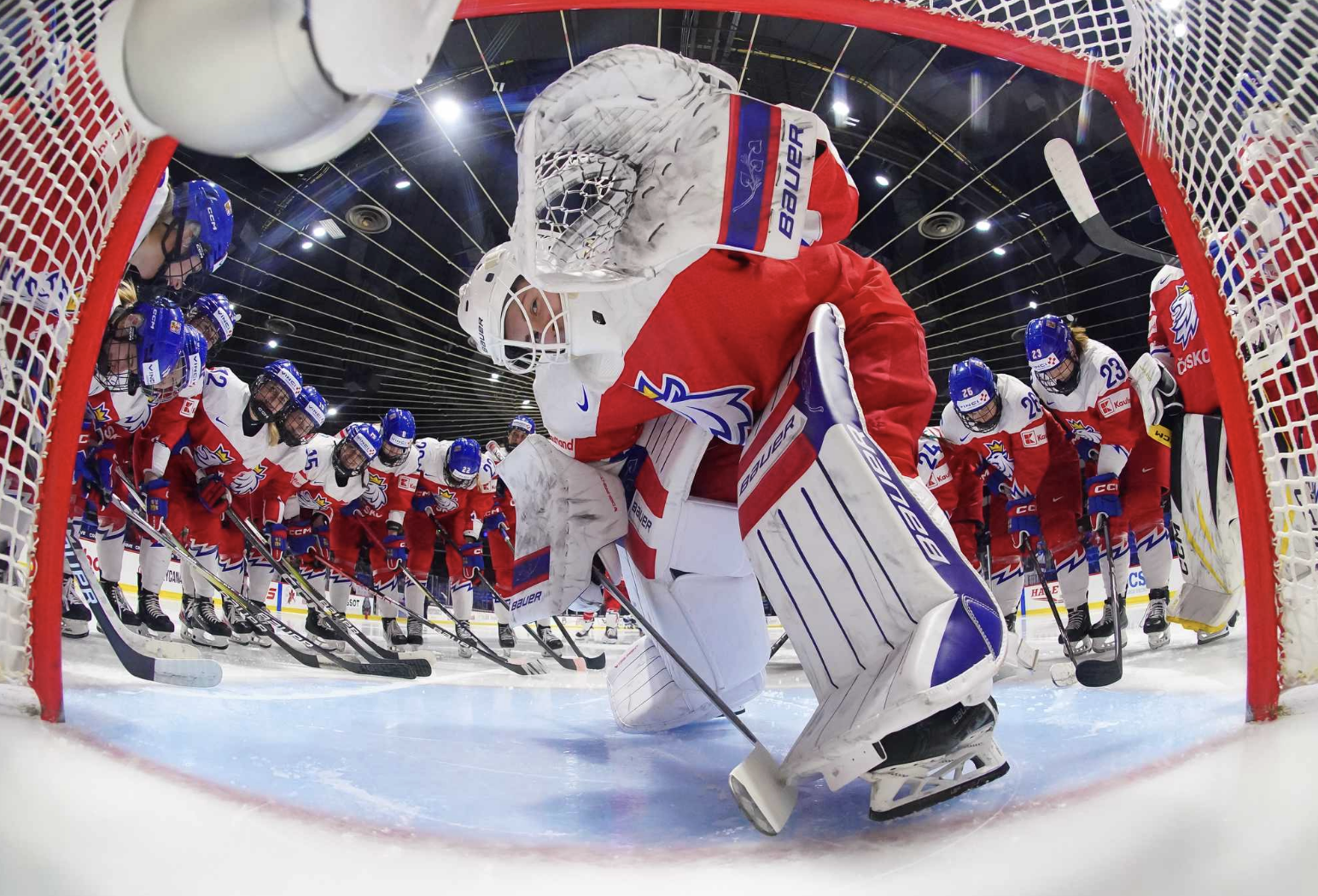 Peslarová bends down to wave at the camera, with her teammates circled up around her. She is wearing a red Czechia uniform.