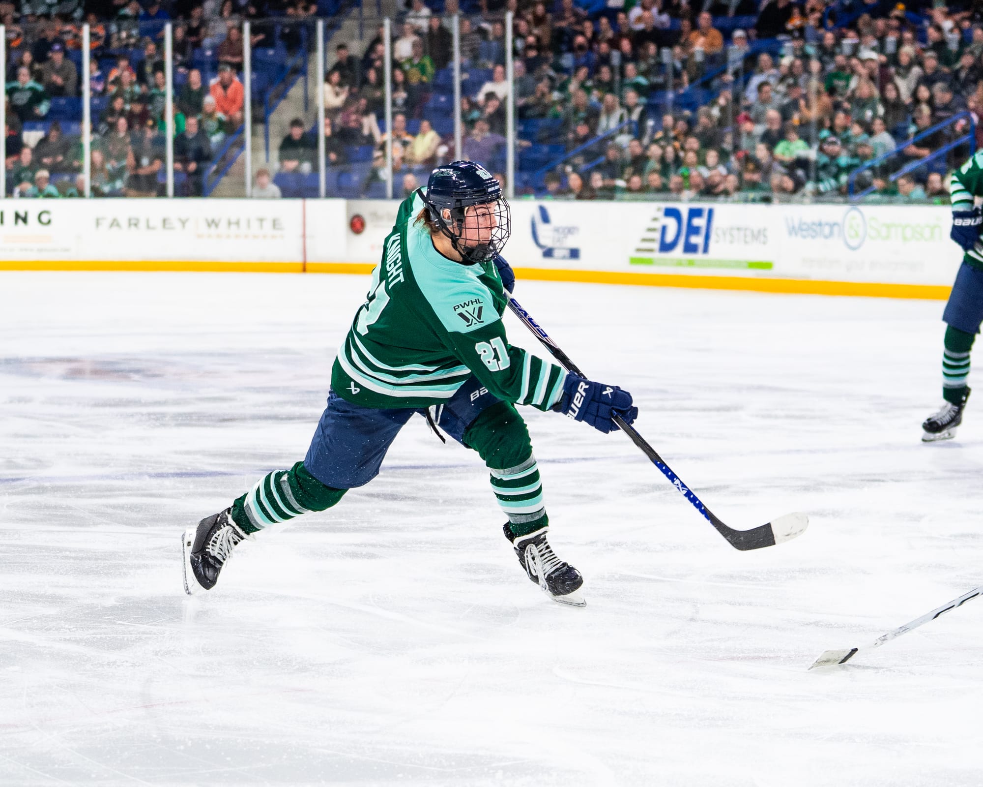 Knight looks ahead and shifts her weight to her left leg as she follows through on a shot. The puck has already left the frame. She is wearing a green home uniform.