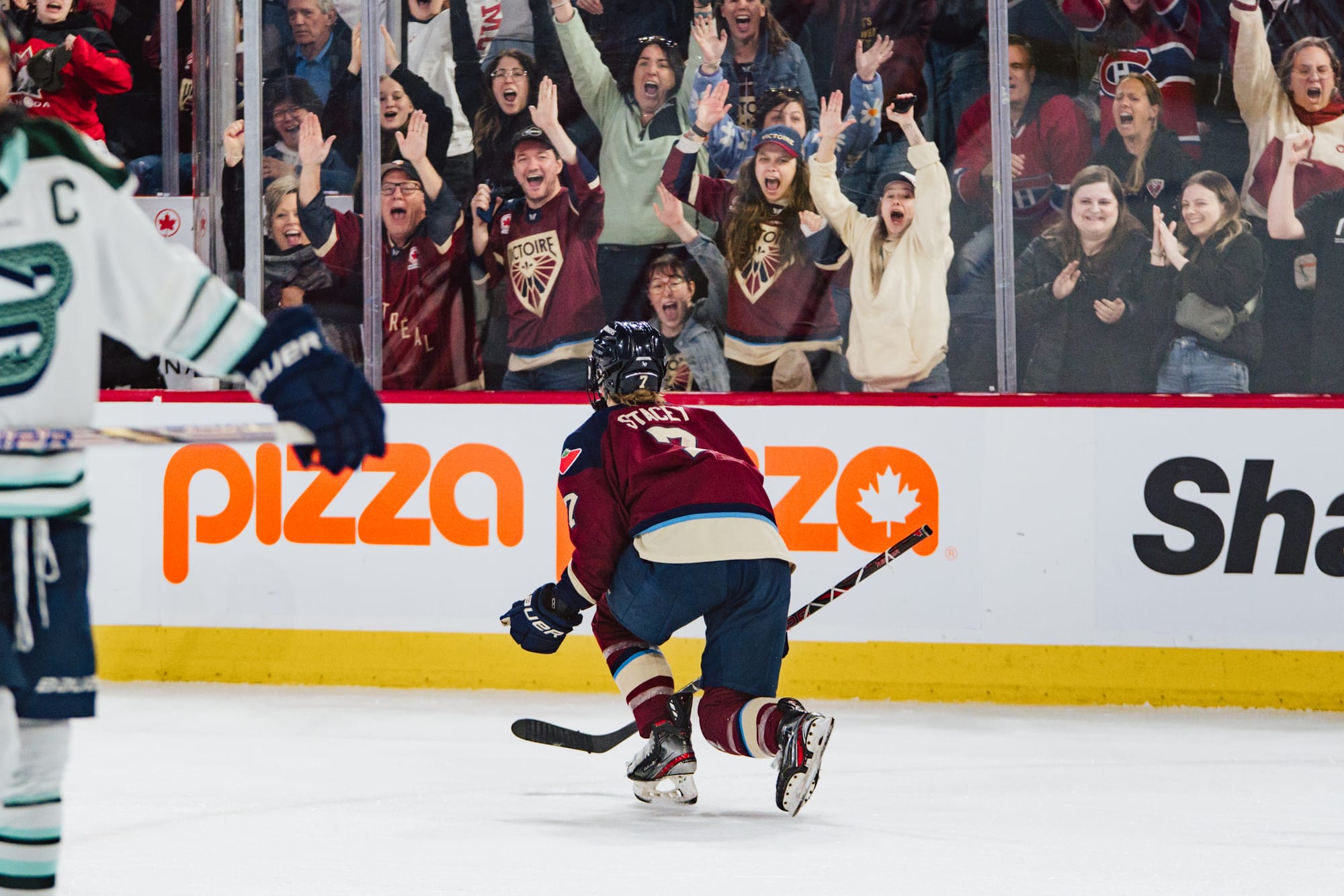 Stacey drops to one knee and pumps her fists in celebration. She is back to the camera and wearing a maroon home uniform. Montréal fans are cheering in the background. 