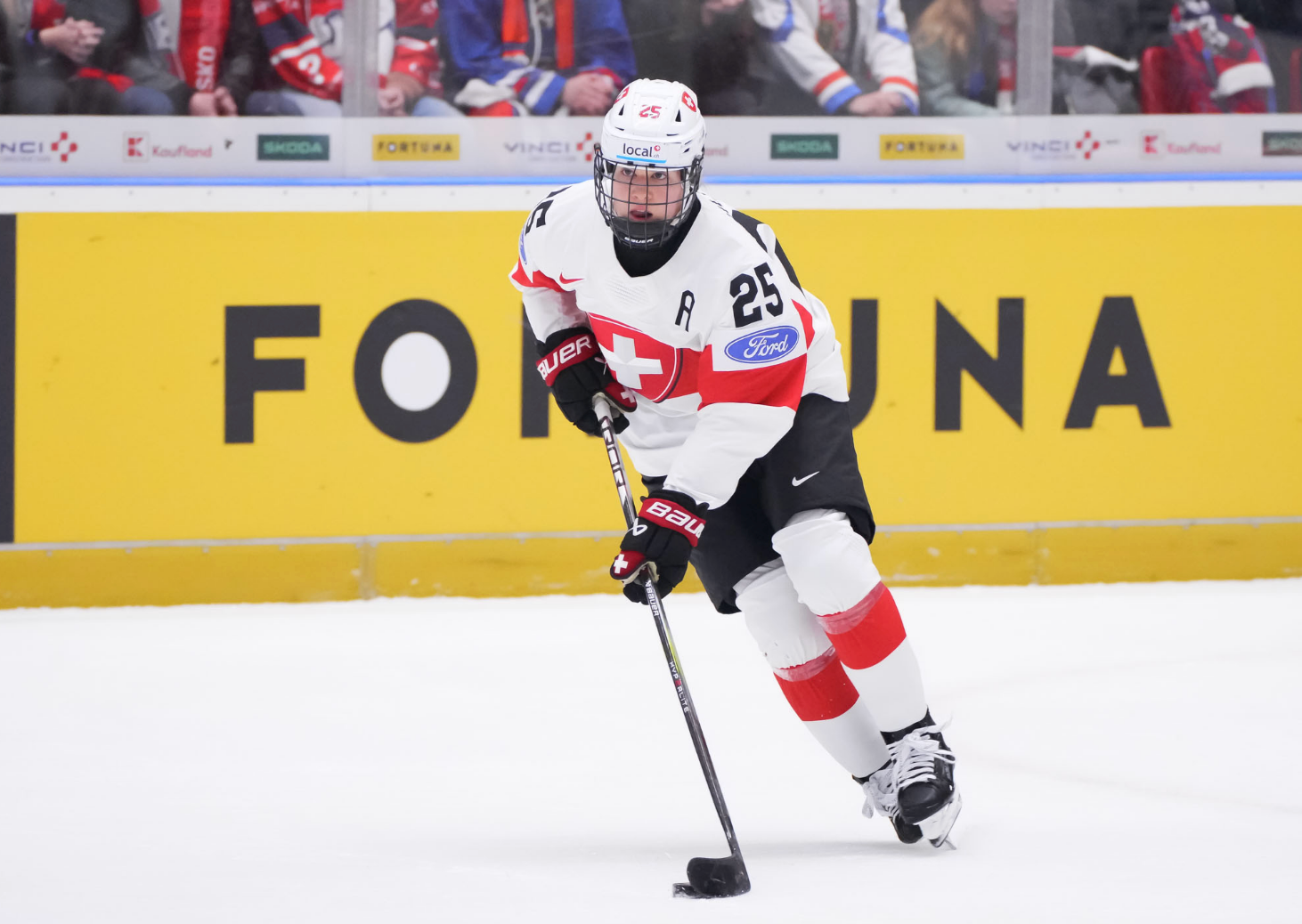 Mรผller looks up as she skates out of the zone with the puck. She is wearing a white uniform.