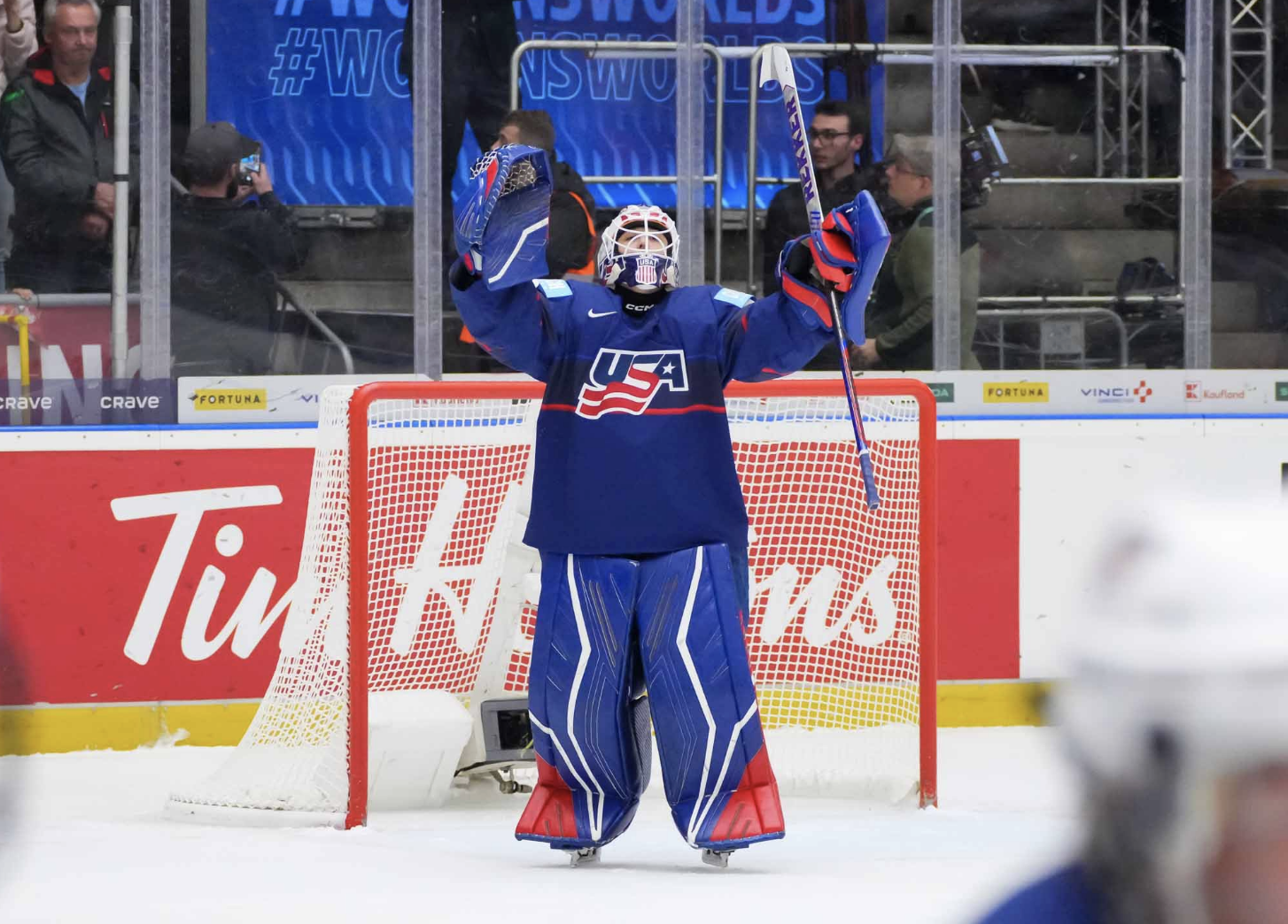 Phillips looks up and raises her hands in celebration. She is wearing a blue uniform and blue pads with red accents in the bottom corner.