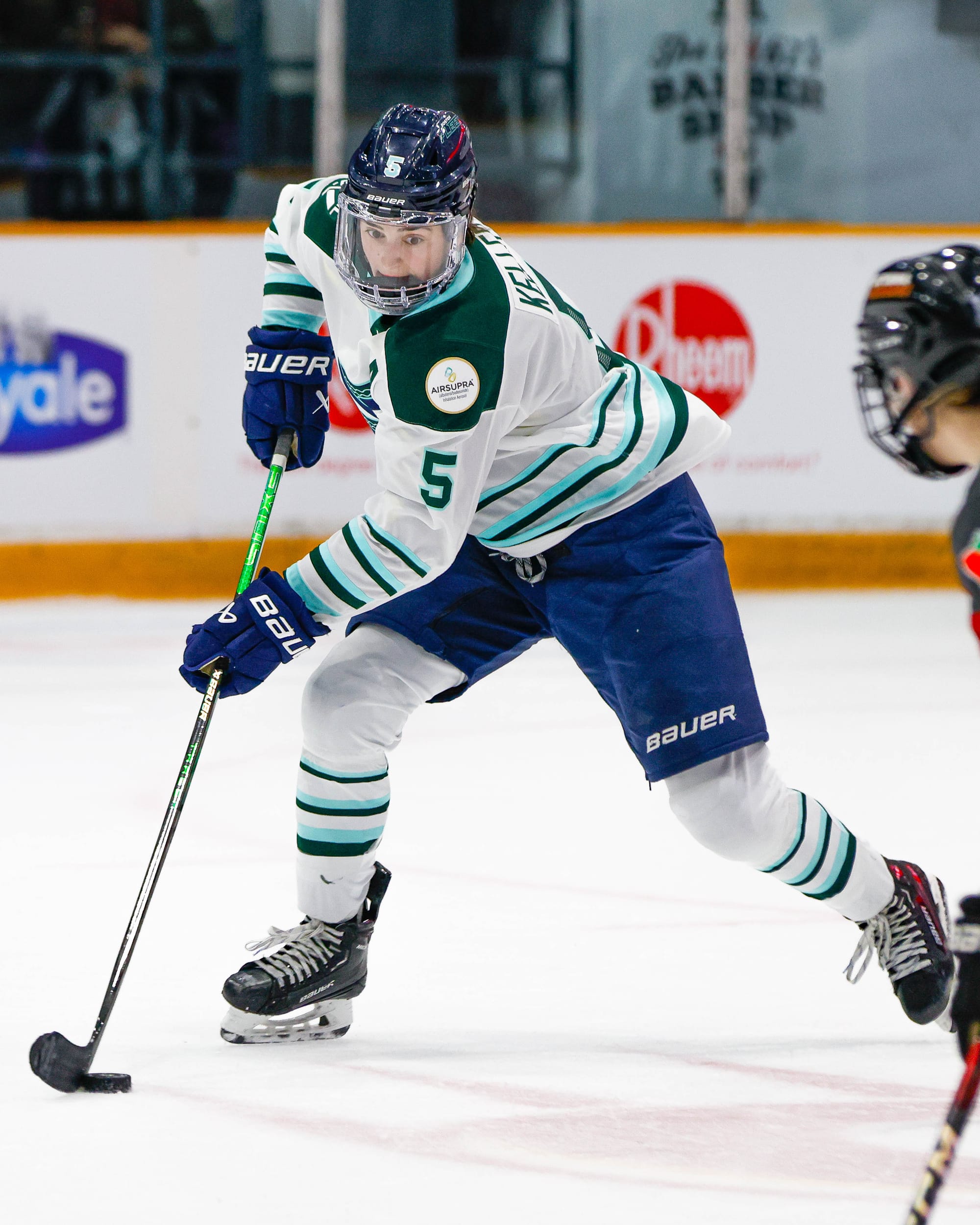 Keller looks down as she protects the puck on her backhand mid-stride. She is wearing a white home uniform.