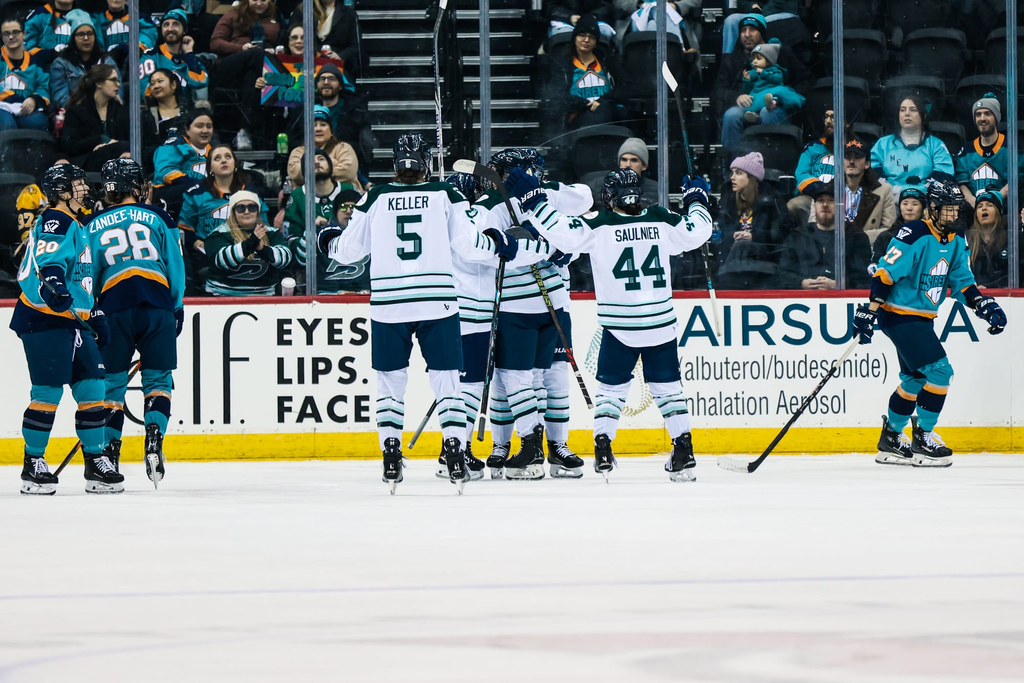 Fleet players celebrate a goal with a group hug. They are wearing white away uniforms.