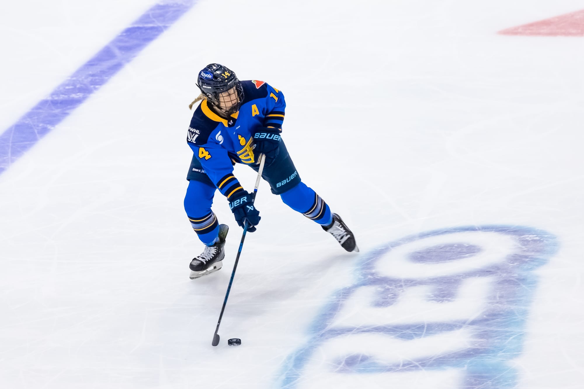 Fast looks to her left as she prepares to make a play with the puck. She is wearing a blue home uniform.