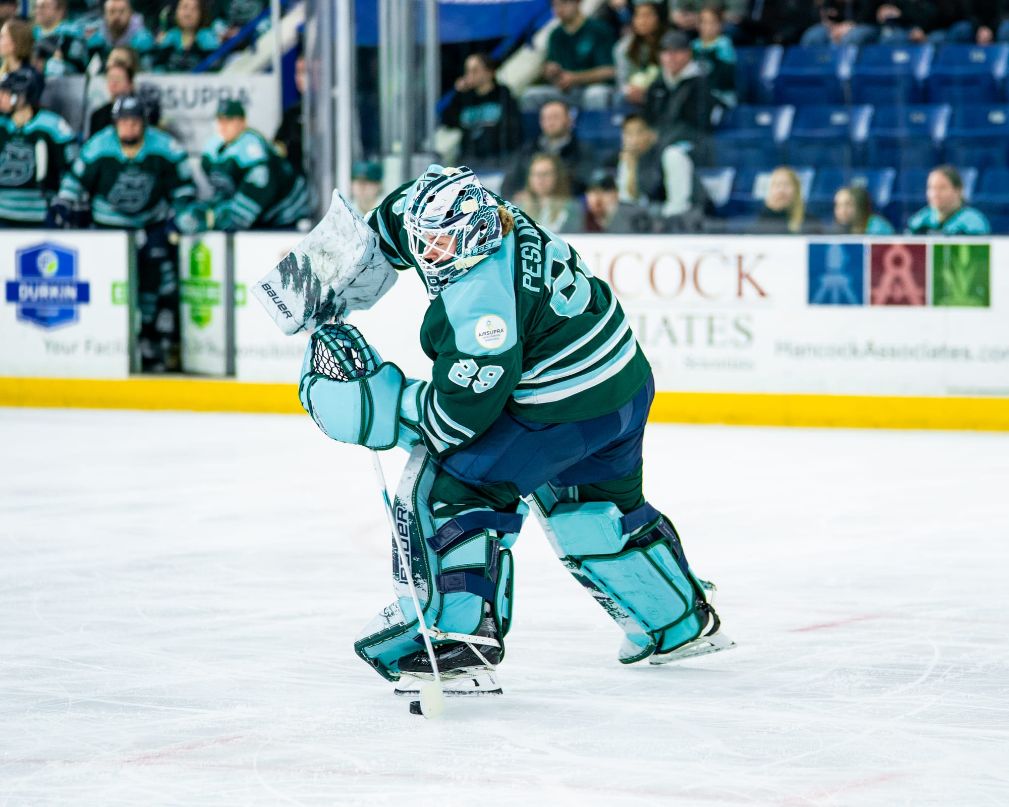 Peslarová leans to her left as she prepares to move the puck up ice. She is wearing a green home uniform.