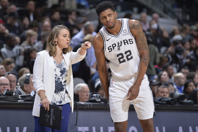 Becky Hammon points out something on the court to Rudy Gay as he leans in to listen, both standing in front of the scorers table,