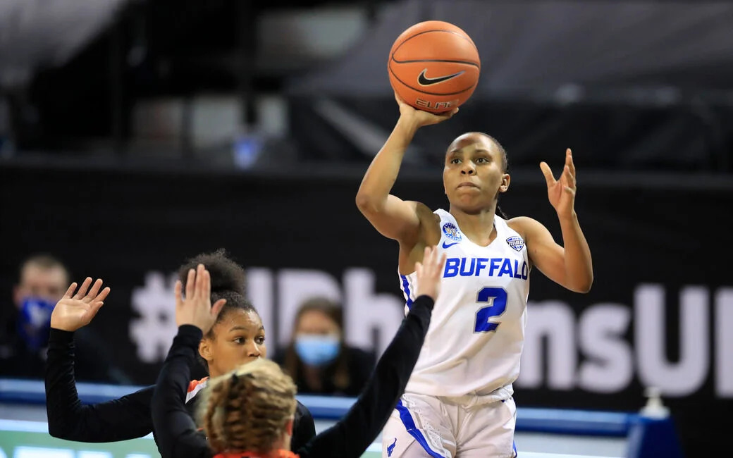 Dyaisha Fair rises midair for a jumper, with her guide hand having left the ball, and a defender attempting to disrupt Fair's shot with their arms.