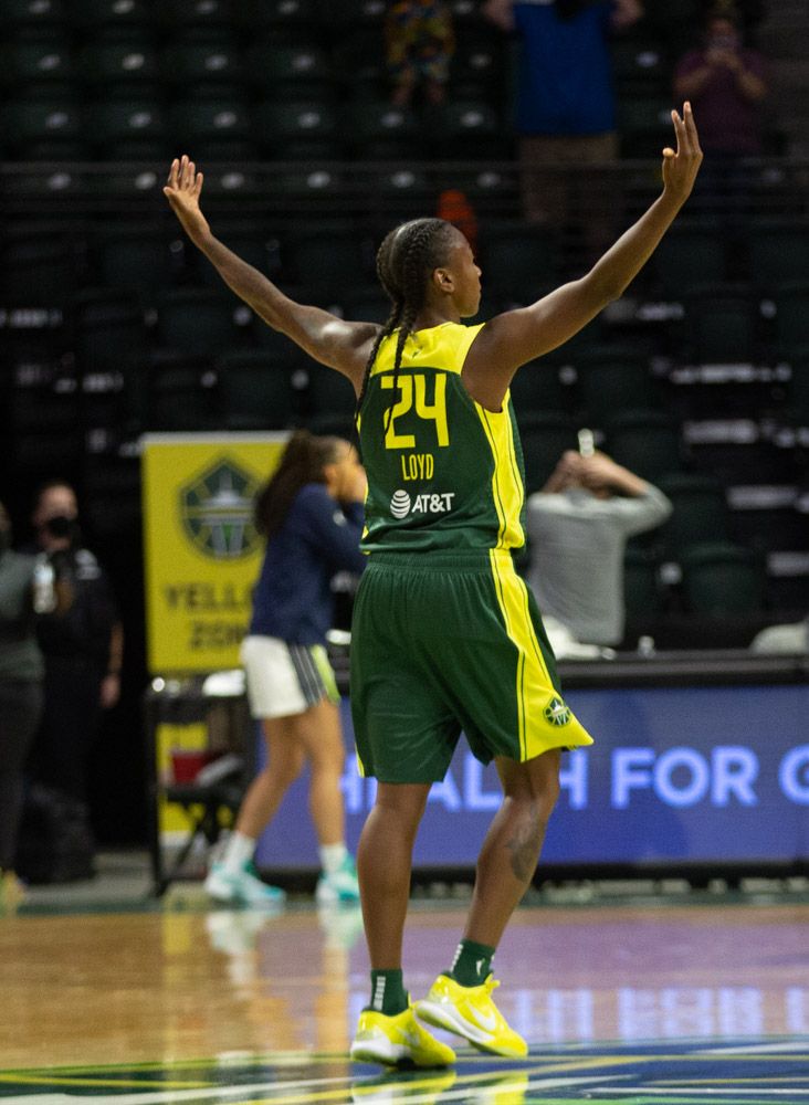 Jewell Loyd, facing away from the viewer, raises her arms to celebrate a miraculous, game-winning, fadeaway, buzzer-beating three. Faintly visible in the background are a completely incredulous Dallas player and random staffer looking downwards with his hands on the back of his head.