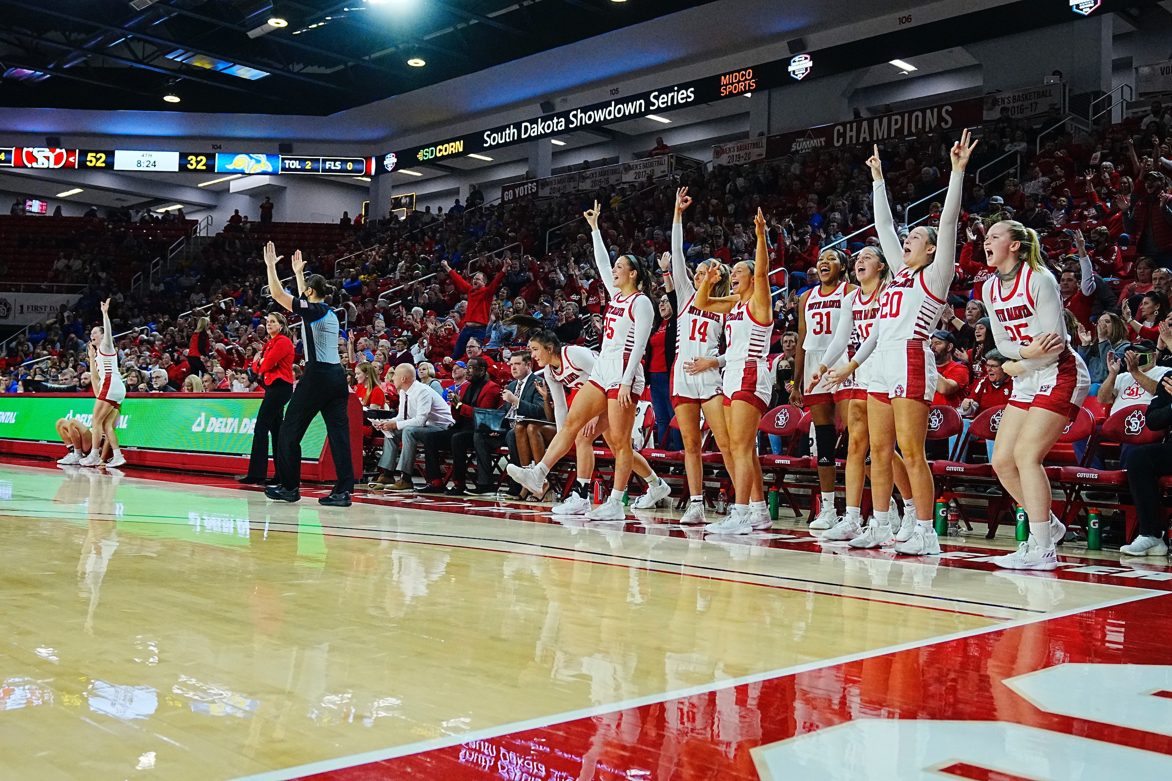 The South Dakota bench and one standing fan (in a sea of many fans) celebrate as a ref signals a three-pointer was good