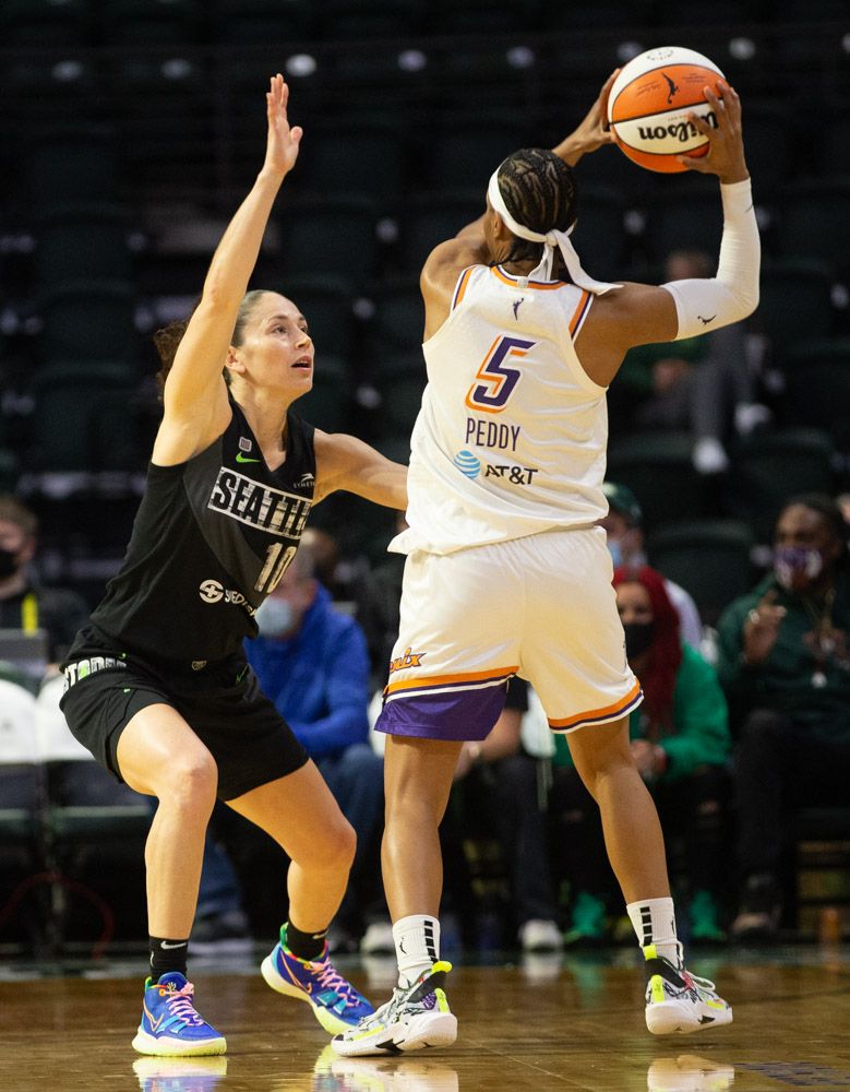Sue Bird face-guards Shey Peddy, whose back is towards the viewer, crouched with her arm straight up as Peddy holds the ball over her own head