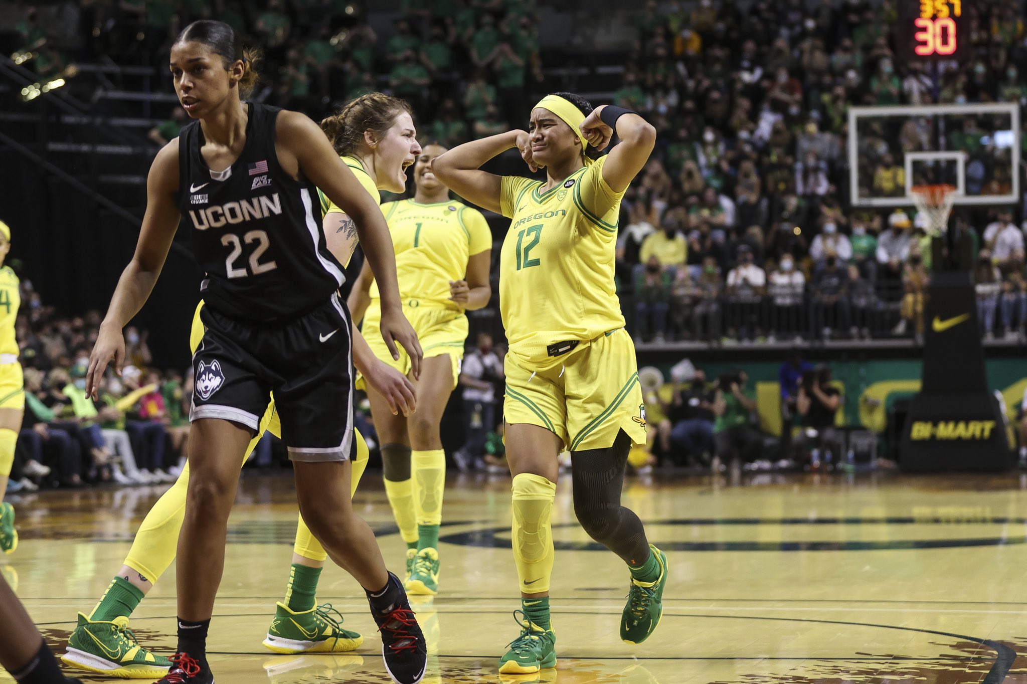 Te-Hina Paopao flexes upwards while walking backwards, Sedona Prince screams at her in celebration next to her, while Nyara Sabally -- visible between them in the background -- smiles wide while backpedaling. In the very foreground, out-of-focus, a UConn player walks towards the hoop.