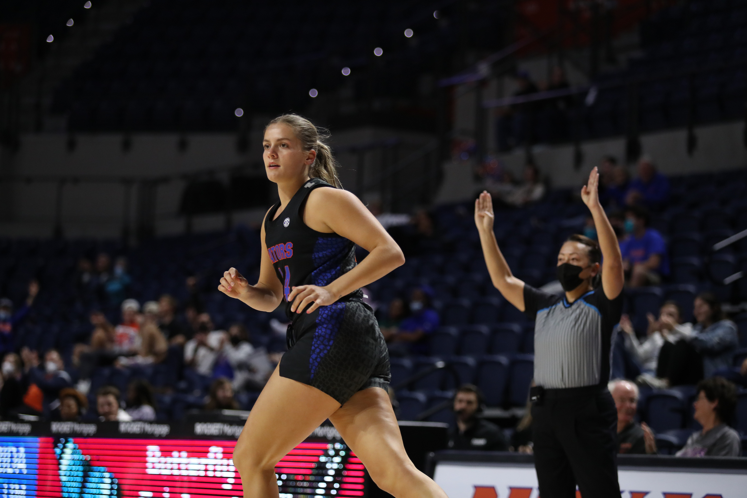 Kristina Moore jogs down the court facing sideways, as a ref behind her signals a made three