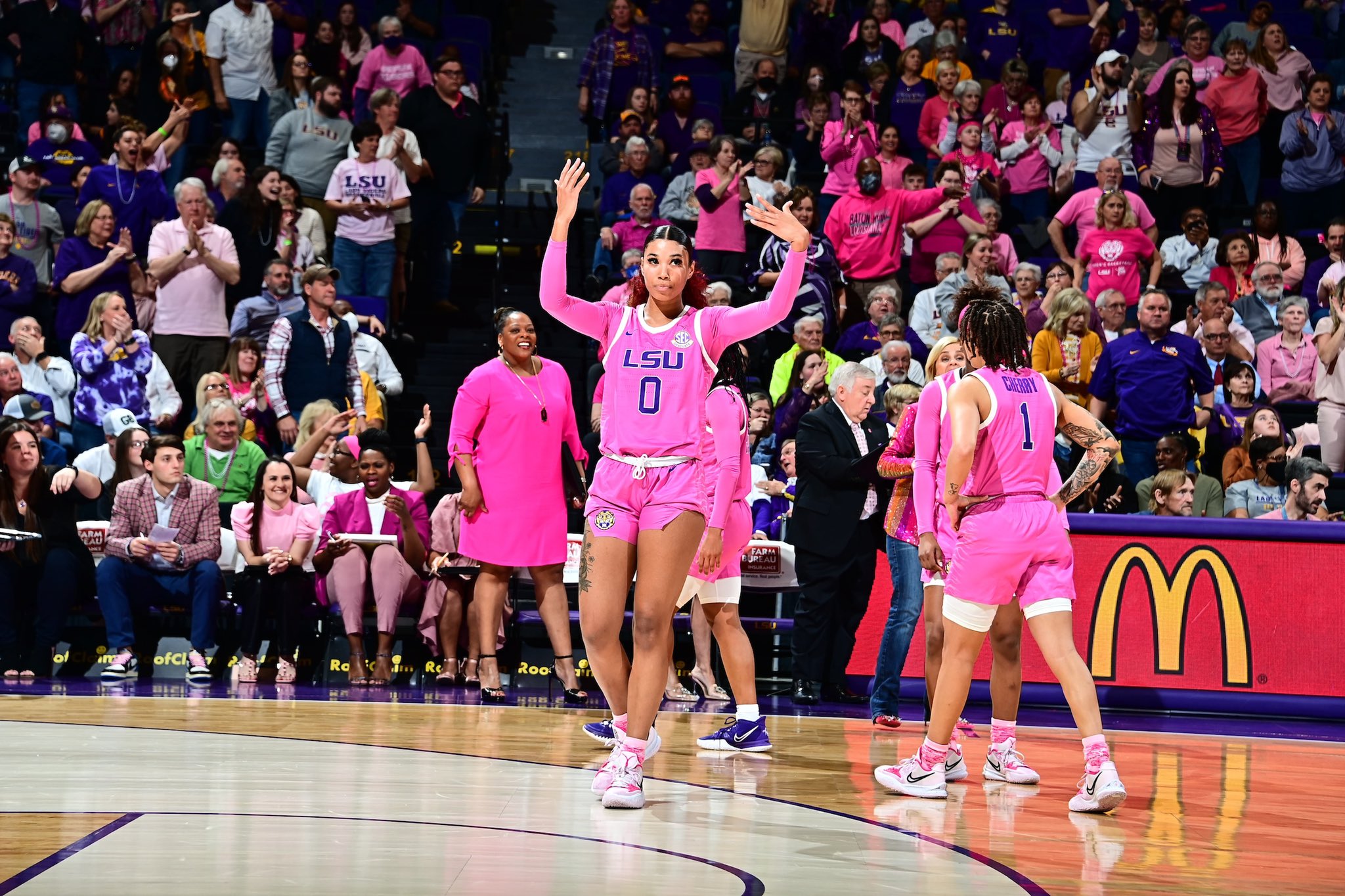 Autumn Newby, facing the camera, motions to the crowd to get louder. Behind her, teammates gather to listen to their head coach.