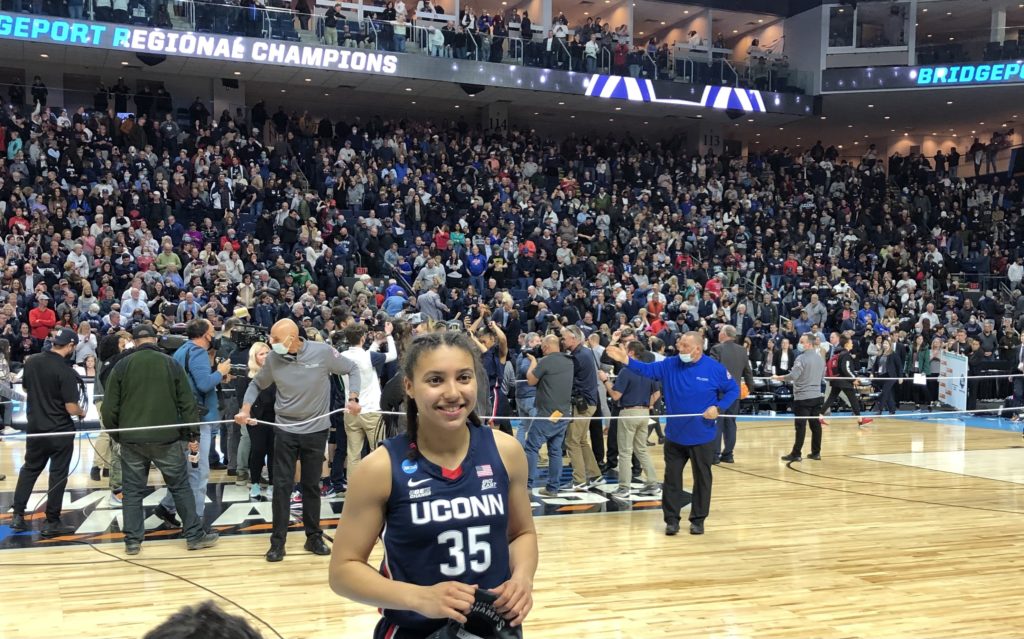 Azzi Fudd of UConn prepares for postgame interview while her teammates celebrate a regional final win, March 28, 2022. (Howard Megdal photo)