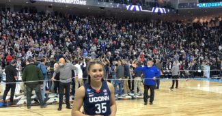 Azzi Fudd of UConn prepares for postgame interview while her teammates celebrate a regional final win, March 28, 2022. (Howard Megdal photo)