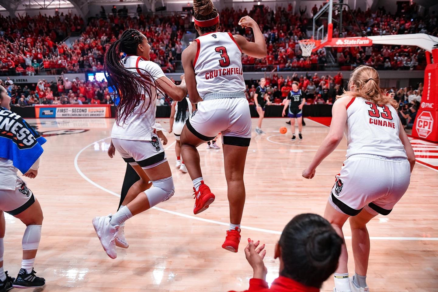 Jakia Brown-Turner, Kai Crutchfield, and Elissa Cunane face away from the camera and towards the court, jumping and celebrating.