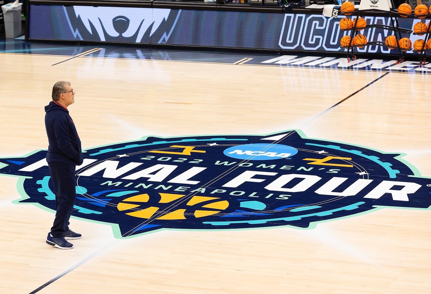 Geno Auriemma stands at halfcourt, but the Final Four logo, looking into the distance, away from the camera