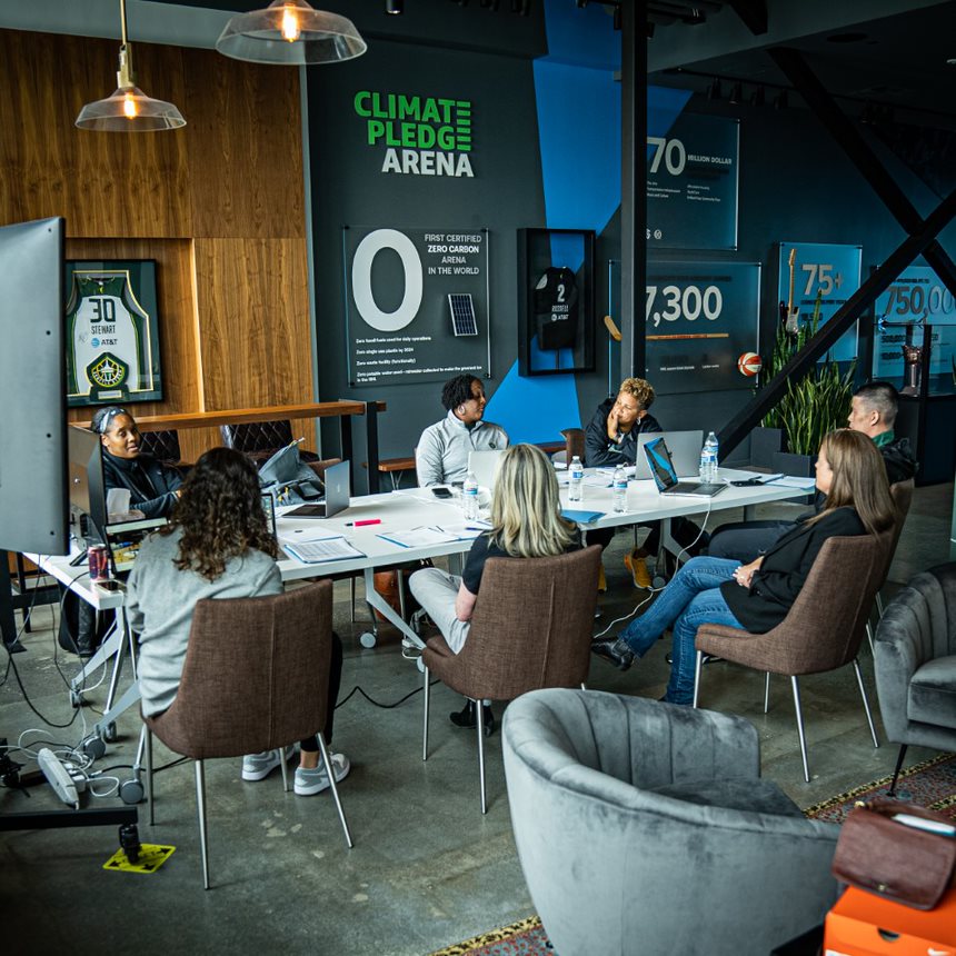 Members of the Seattle Storm front office and coaching staff sit around a table littered with papers, laptops, and office supplies for the 2022 WNBA Draft.
