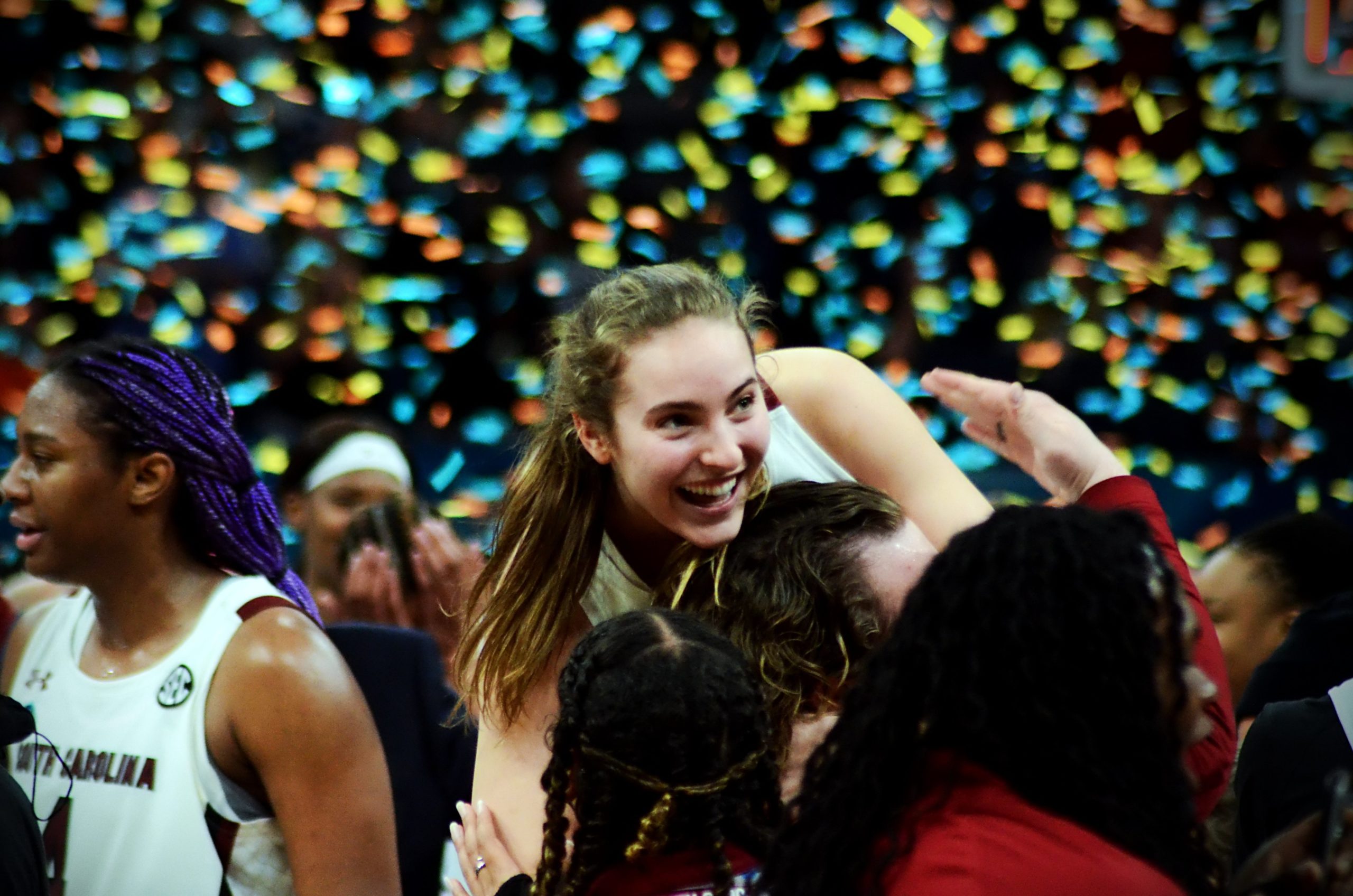 Among a mess of bodies, Olivia Thompson hangs on a South Carolina staffer, smiling widely while looking to the right of the viewer, while confetti rains down in the background