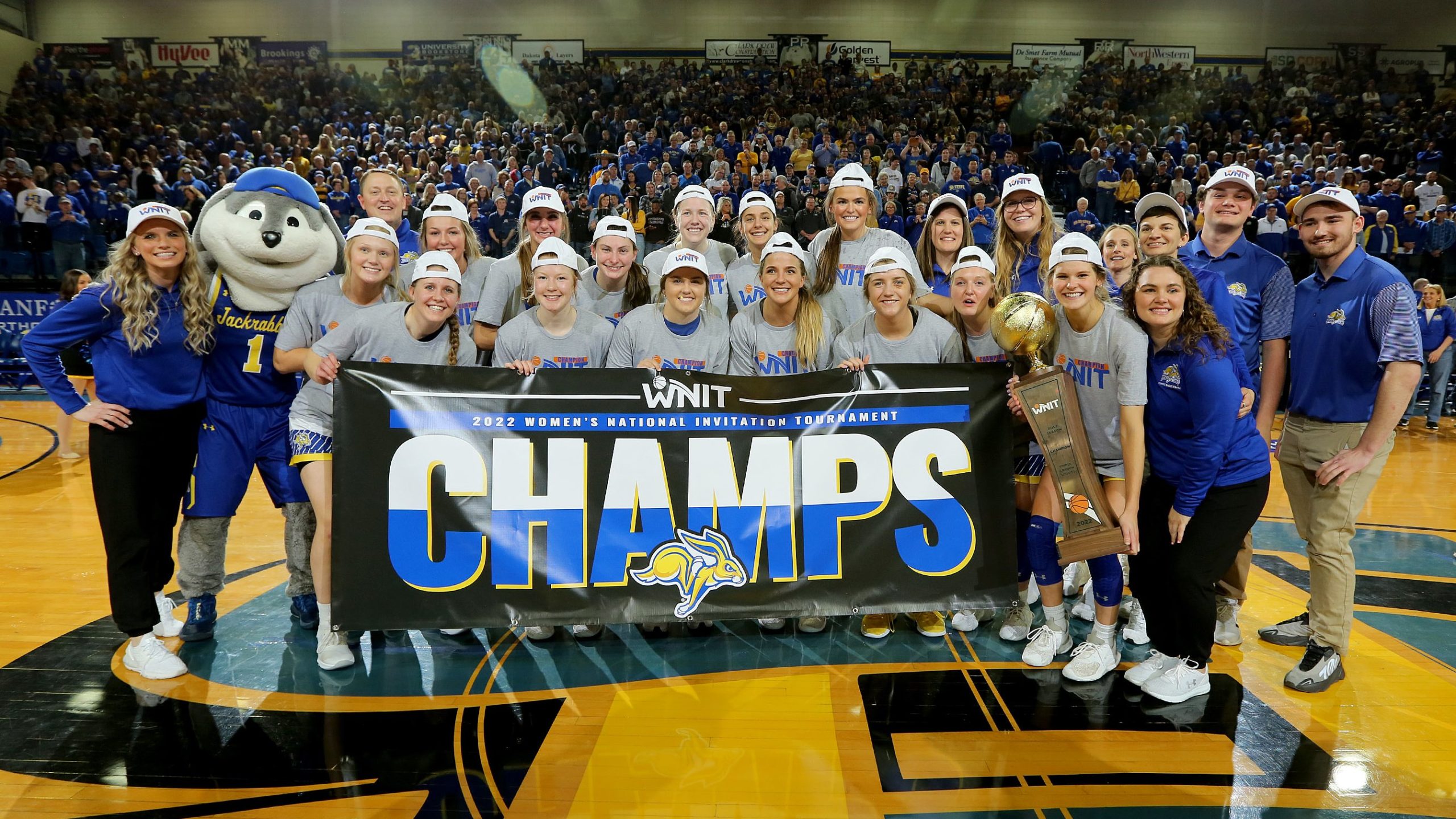South Dakota State players and coaches gather around a WNIT championship banner with the tournament trophy