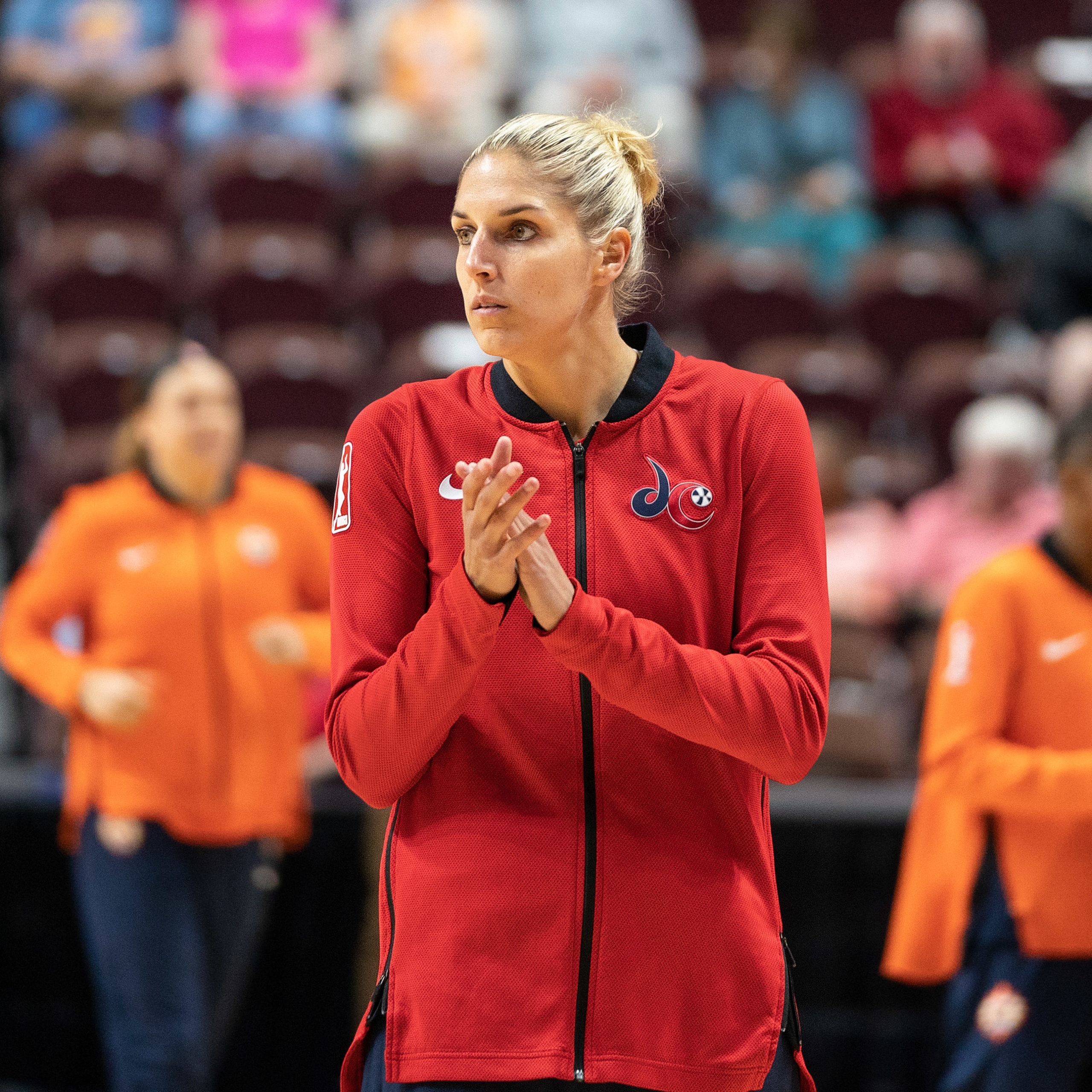 Washington Mystics forward Elena Delle Donne wears a red Mystics warm-up jacket. She clasps her hands together and looks off to the side.