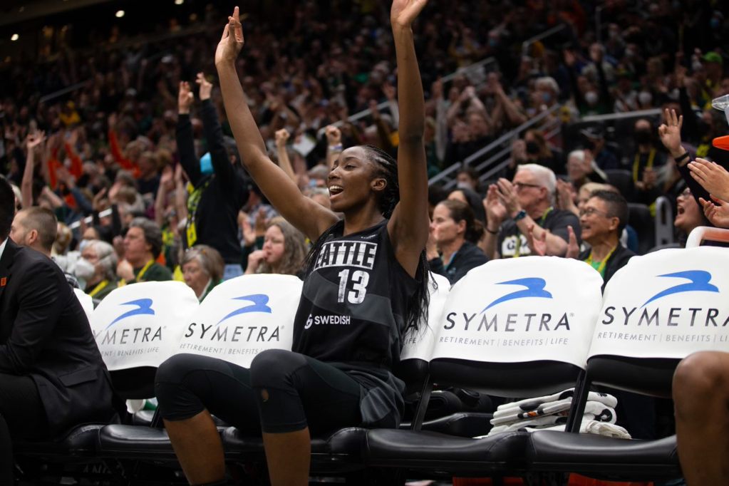 Seattle Storm big Ezi Magbegor celebrates a teammate's three from the bench, while the crowd celebrates in the background