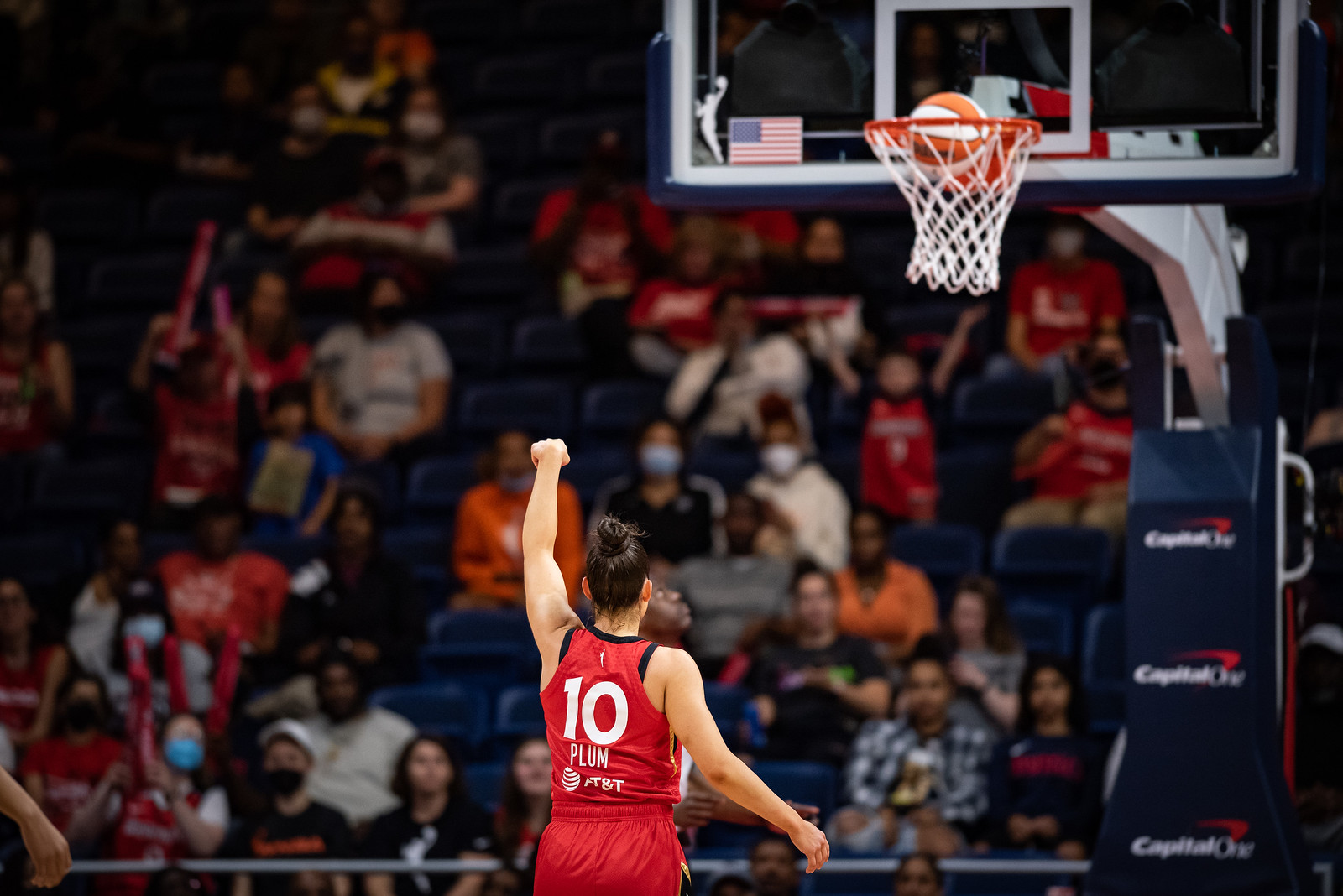 A shot of Las Vegas point guard Kelsey Plum from behind, holding her follow-through as the ball falls through the hoop. Fans in the background celebrate but are out of focus.