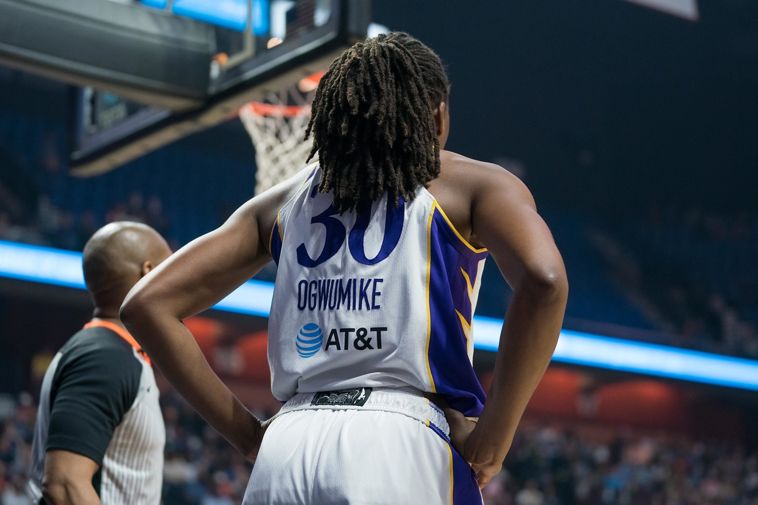 Los Angeles Sparks big Nneka Ogwumike looks out at the court from the baseline behind the basket, as a ref stands next to her