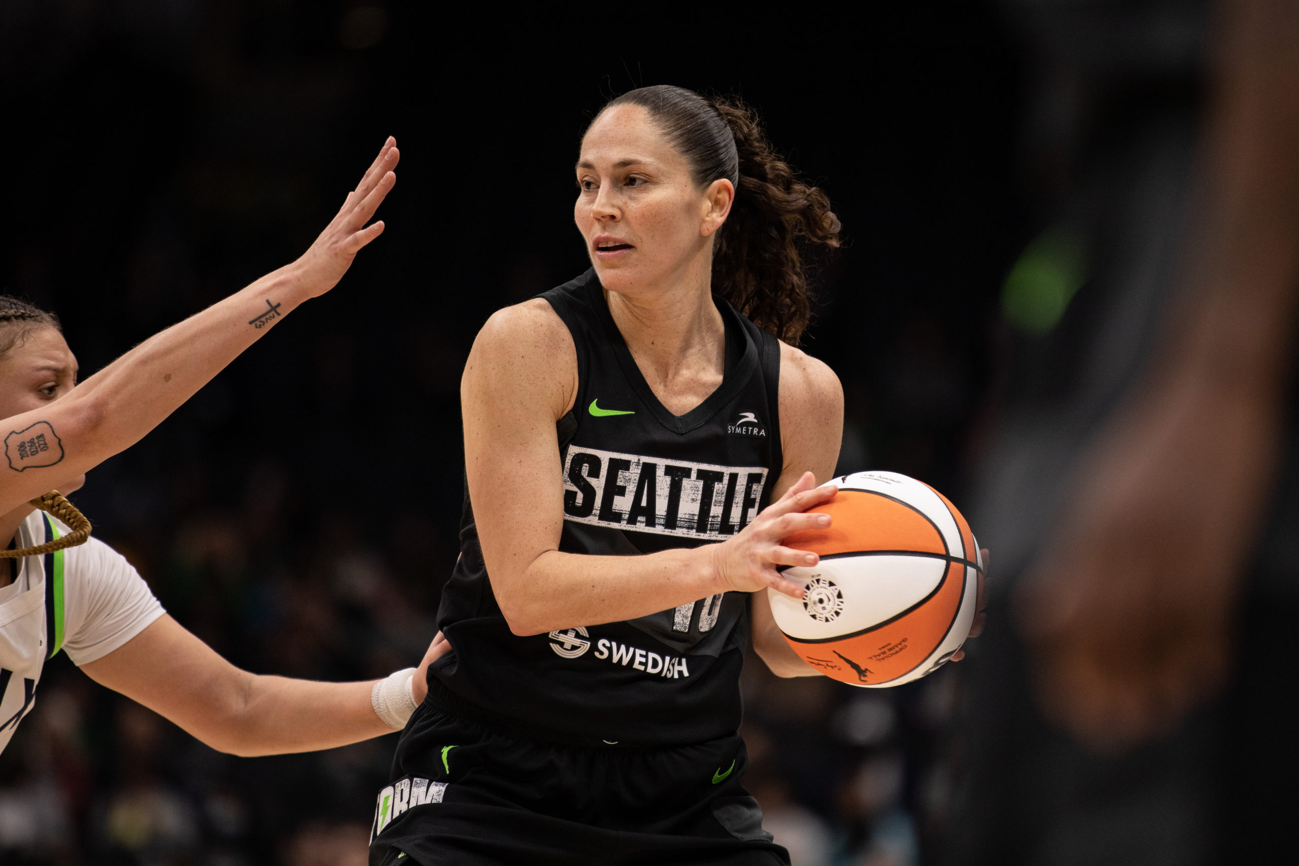 Seattle Storm point guard Sue Bird holds the ball away from a defender's arms while looking to pass