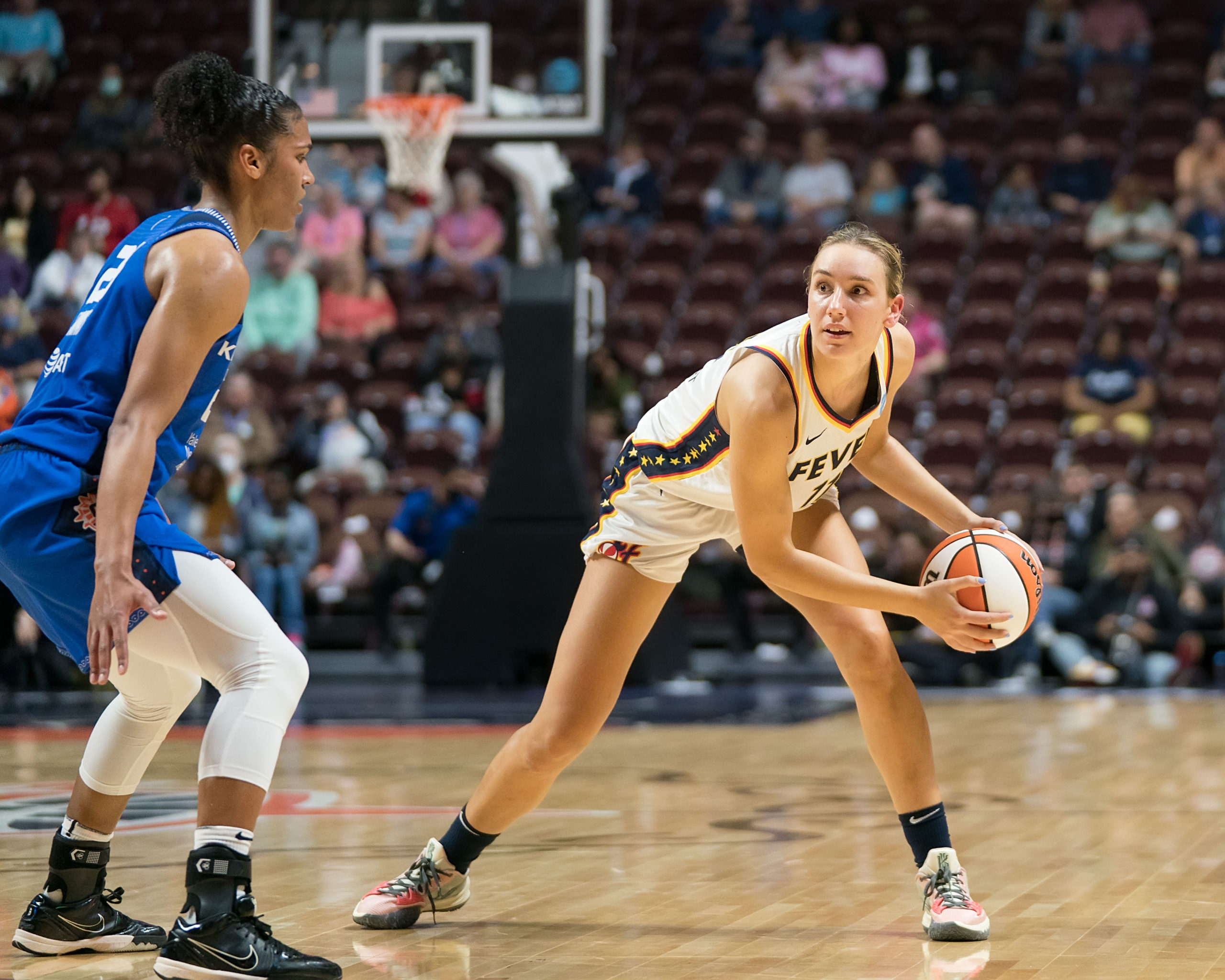 Indiana Fever big Alanna Smith holds the ball beyond the arc while looking upcourt for a passing option, as Connecticut Sun big Alyssa Thomas guards her