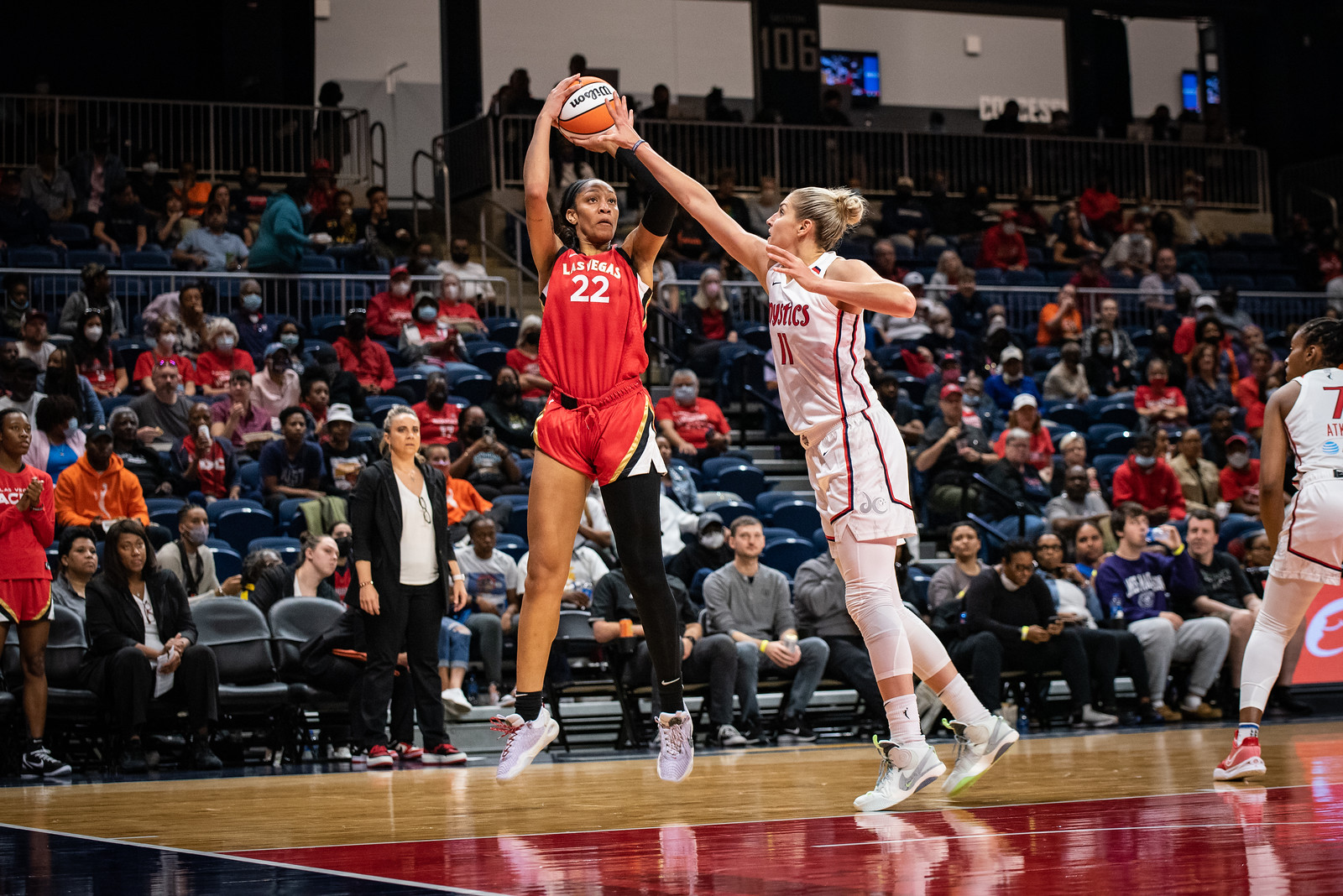 Las Vegas Aces center A'ja Wilson has the ball above her head in mid-air just before releasing a jumper from the low post, as Washington Mystics big Elena Delle Donne jumps towards her with her arm out to try to block the shot