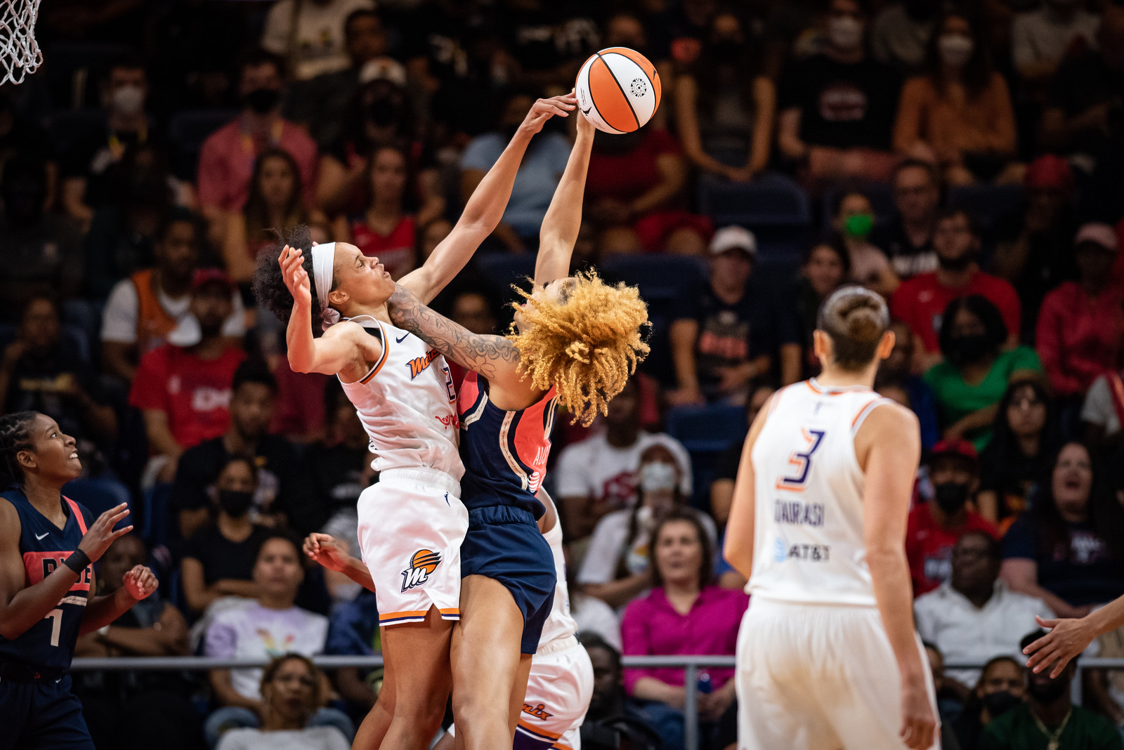 Phoenix Mercury big Brianna Turner jumps into the body of Washington Mystics center Shakira Austin with an arm outstretched and blocking the ball out of Austin's hand, while Austin's other arm tries to keep Turner away