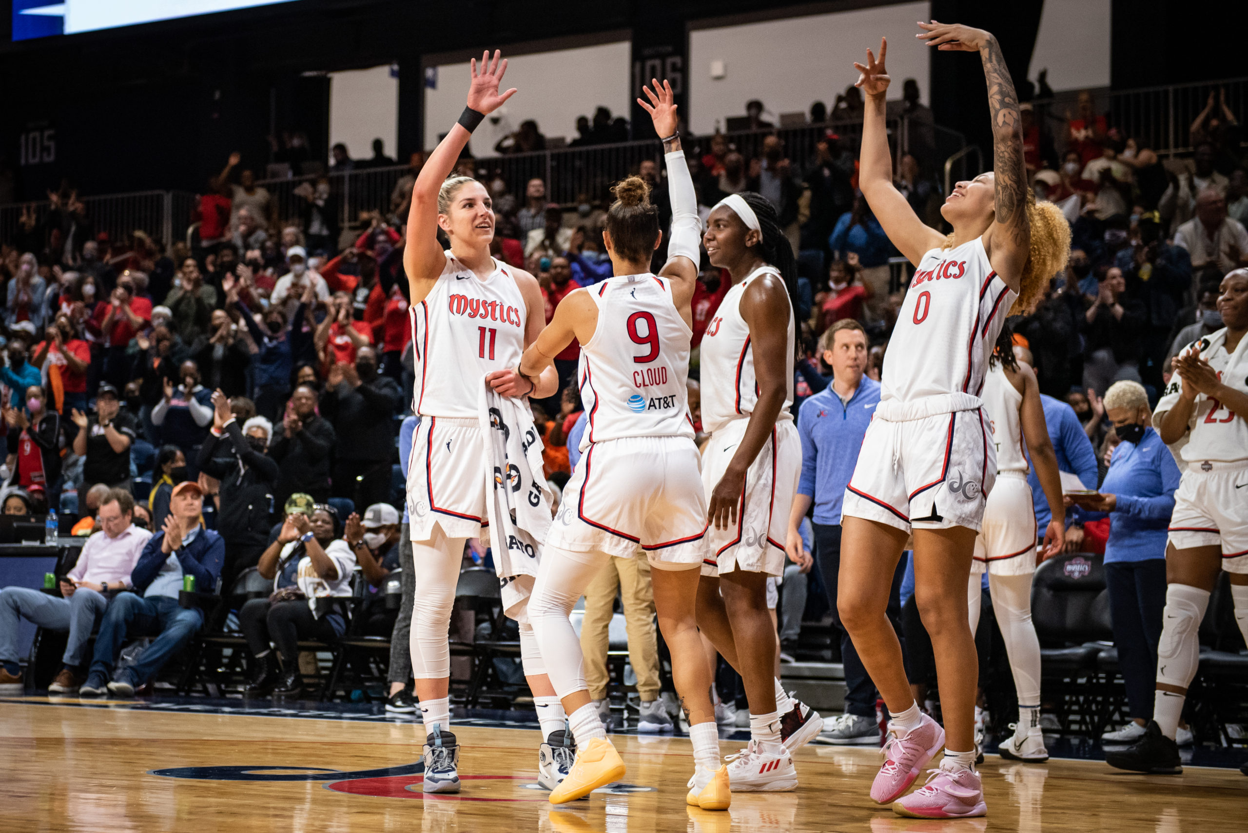 Washington Mystics forward/guard Elena Delle Donne waves to the crowd near the Mystics' bench after scoring her 4,000th career point. Teammate Natasha Cloud eggs the crowd on with one hand, and Shakira Austin celebrates nearby.