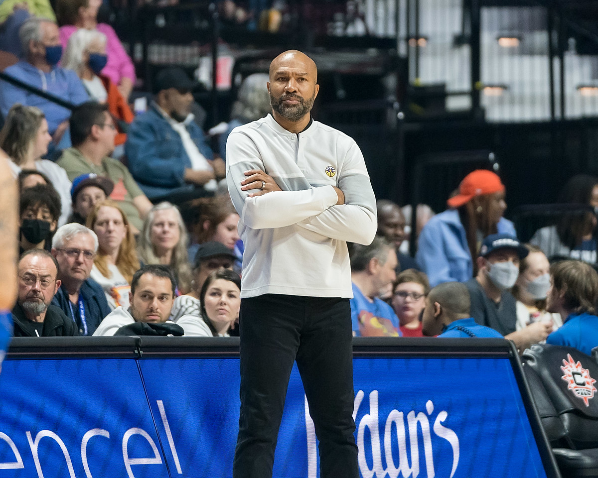 Los Angeles Sparks head coach Derek Fisher stands in front of the scorer's table, looking out towards the court with his arms crossed