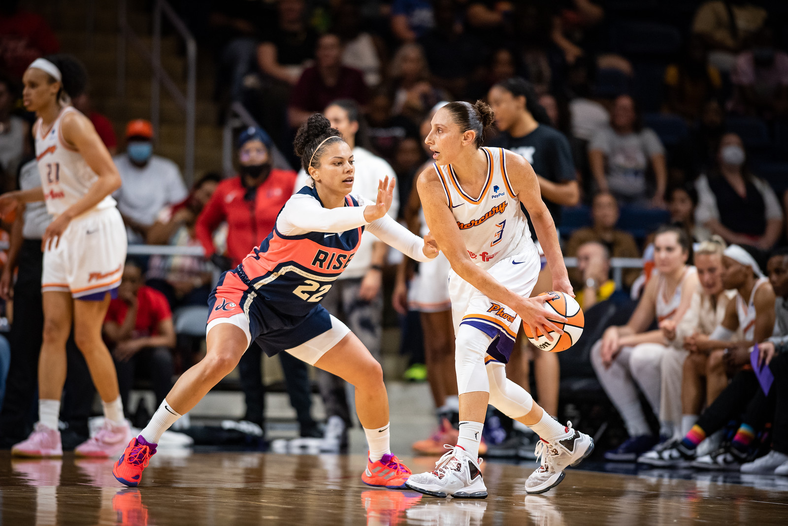 Diana Taurasi stands at the slot while looking across the court with the ball held behind her upcourt hip, as Washington Mystics off-ball guard Alysha Clark crouches in a defensive stance directly in front of her with a hand in front of Taurasi to obstruct a possible pass