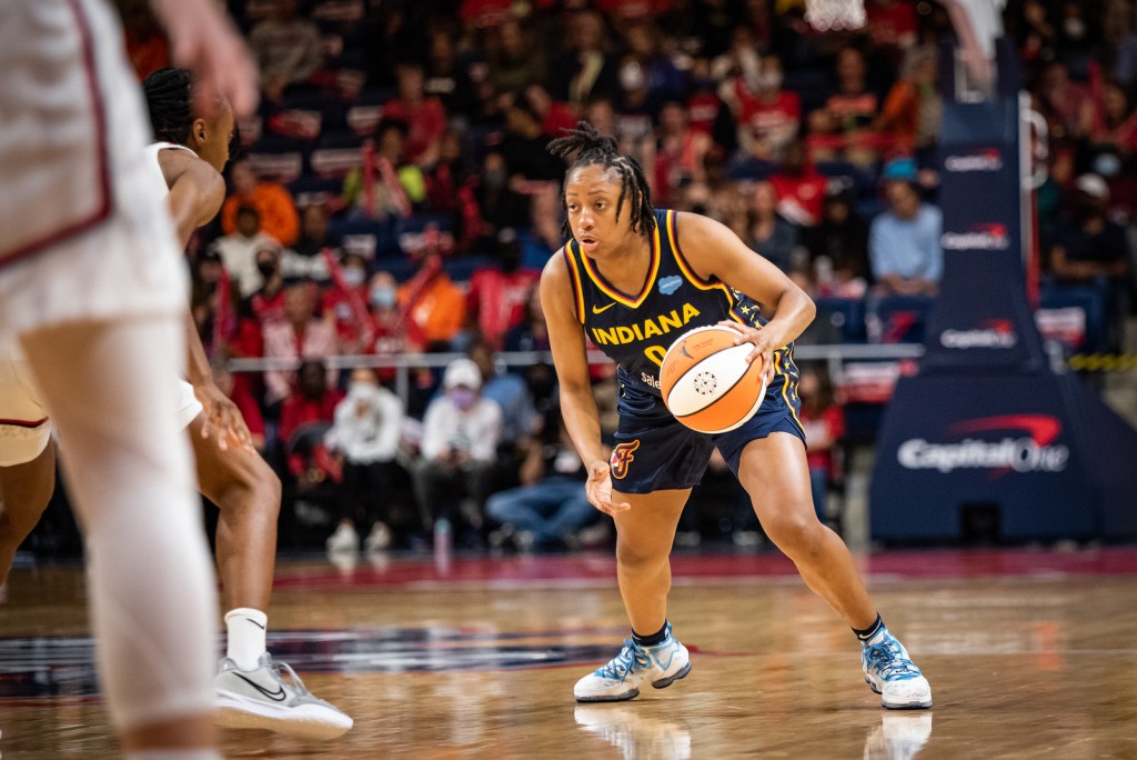 A crouched Indiana Fever point guard Kelsey Mitchell has the ball at the top of her dribble, while looking down the court