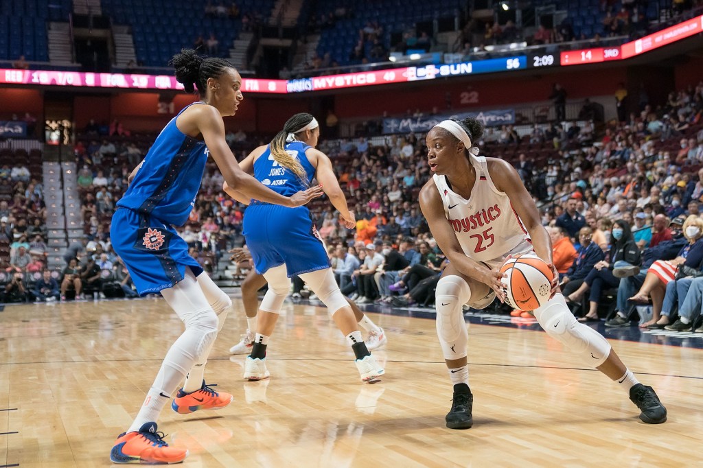 Washington Mystics combo forward Kennedy Burke, surveying the court, holds the ball at her hip in a three-point stance near the short corner, as Connecticut Sun big wing DeWanna Bonner stands a foot in front of her to defend