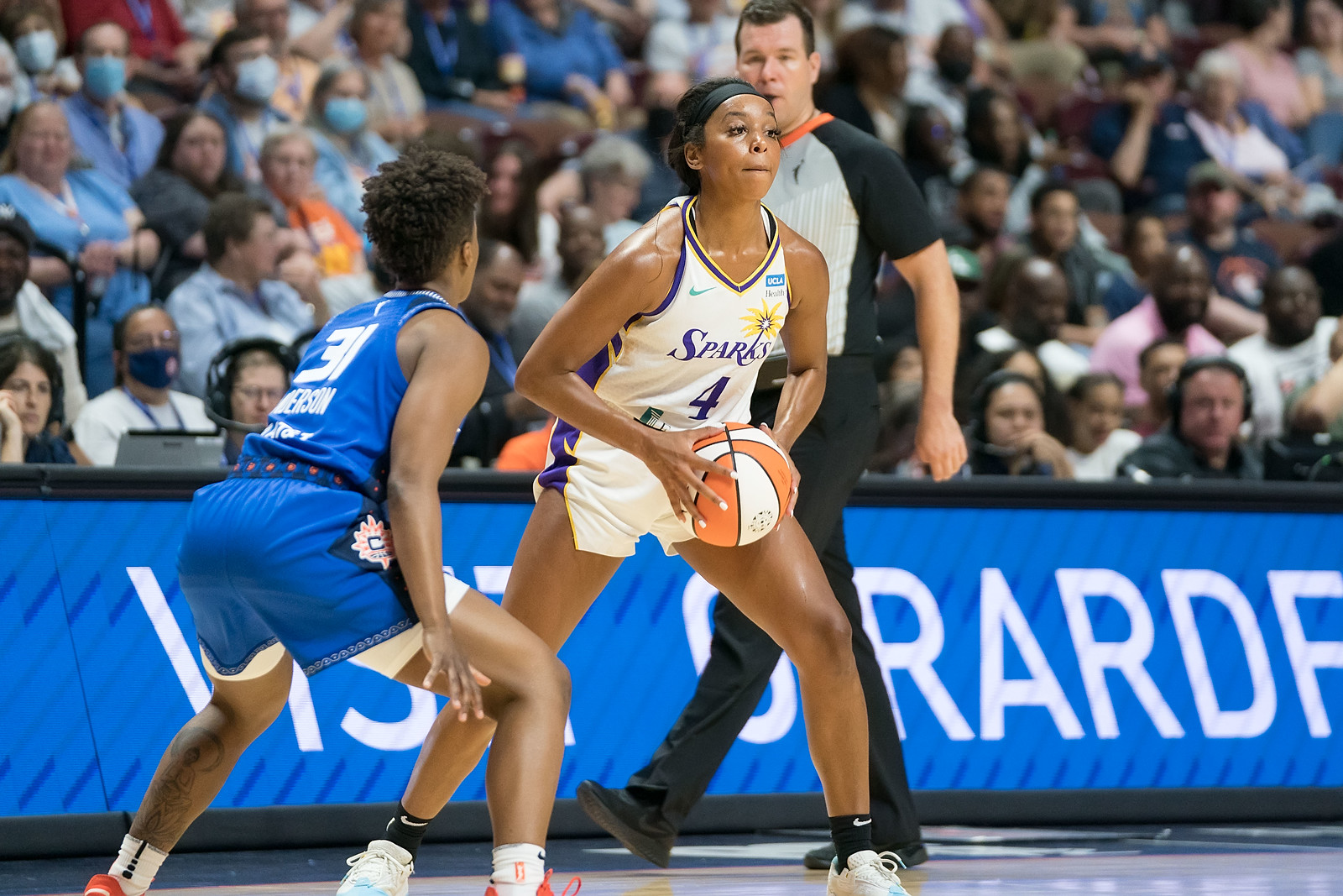 At the slot, Los Angeles Sparks off-ball guard Lexie Brown looks towards the key and gathers the ball at her hips to pass, while Connecticut Sun point guard Yvonne Anderson stands right in front of her to defend