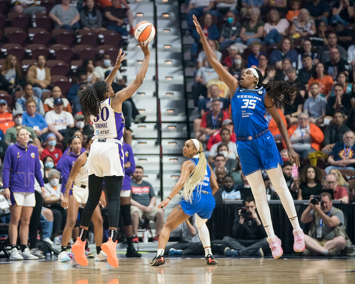 Los Angeles Sparks big Nneka Ogwumike releases a three-pointer from the slot off her fingertips, as Connecticut Sun big wing Jonquel Jones jumps towards her with an outstretched arm to try to block the shot