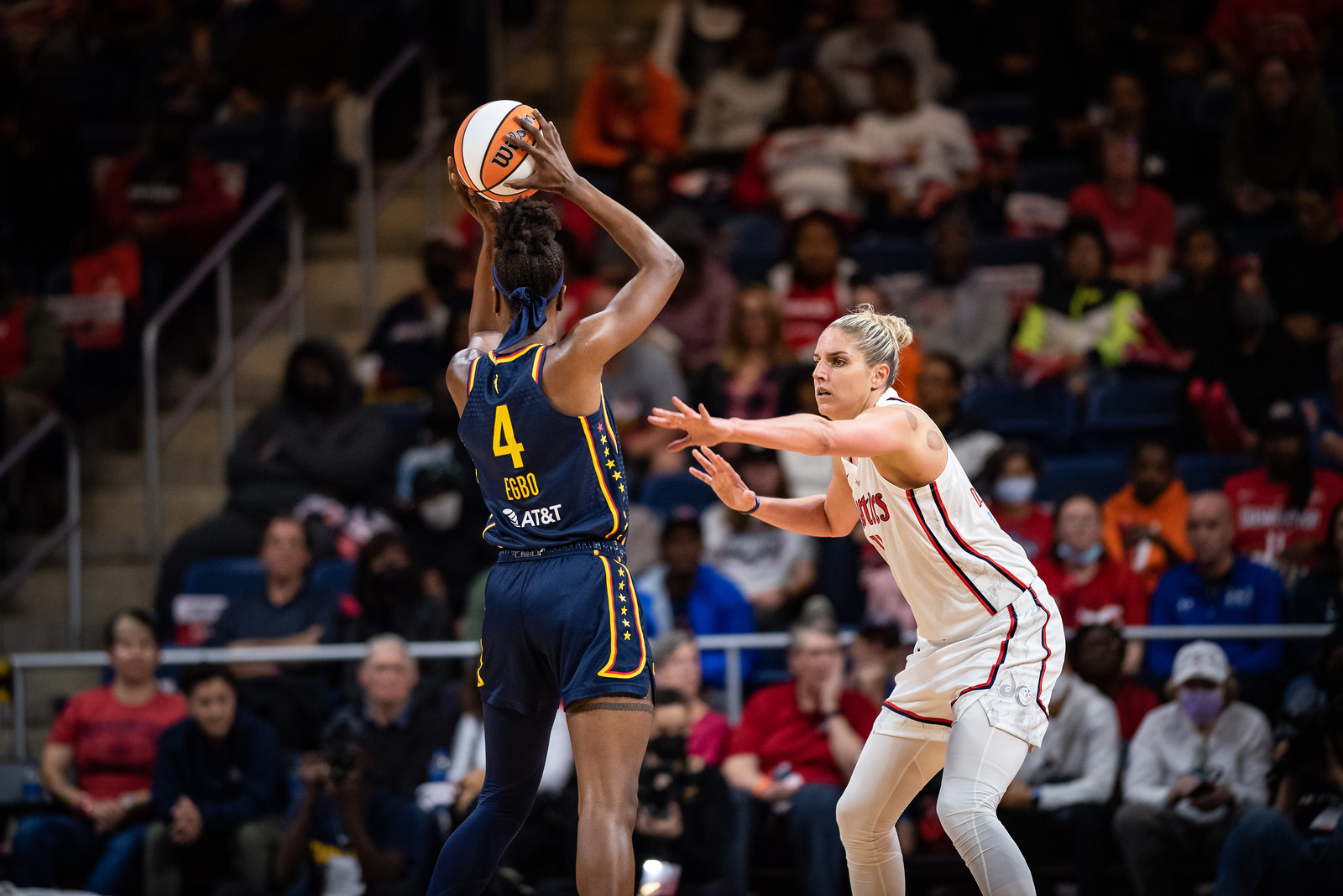 Indiana Fever center Queen Egbo holds the ball above her head while looking upcourt, as Washington Mystics big Elena Delle Donne holds an arm towards her to defend.