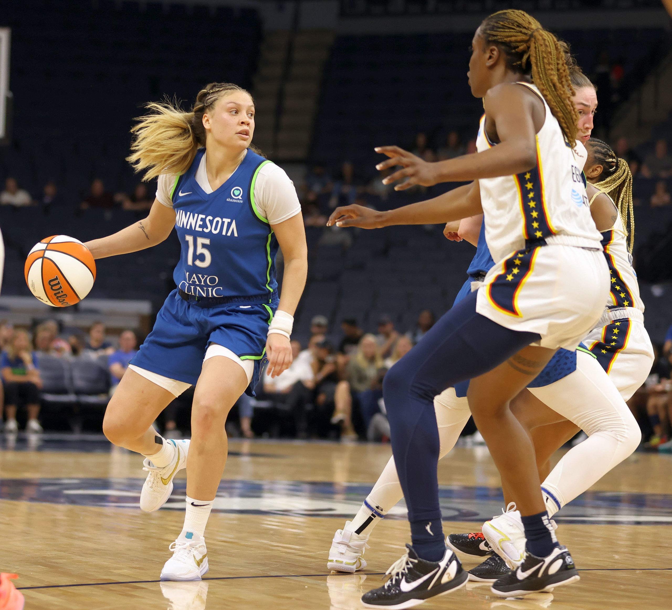 Minnesota Lynx combo guard Rachel Banham dribbles at the slot while looking across the court, a teammate dives on a 45 cut and two Indiana Fever defenders stand in front of Banham