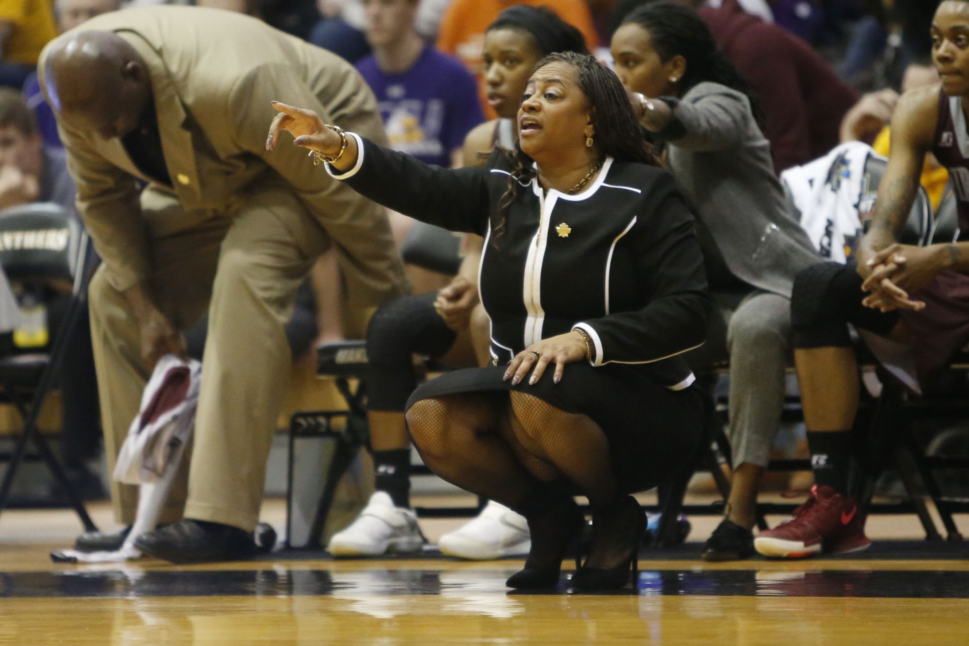 Coach AnnMarie Gilbert crouches on the sideline, pointing out towards the court