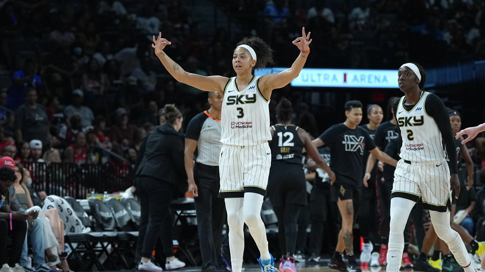 Chicago Sky forward/center Candace Parker walks up the court while flashing the "three" symbol with both hands. Sky wing Kahleah Copper walks up confidently behind her, and Las Vegas Aces players walk away from them towards the bench for a huddle.