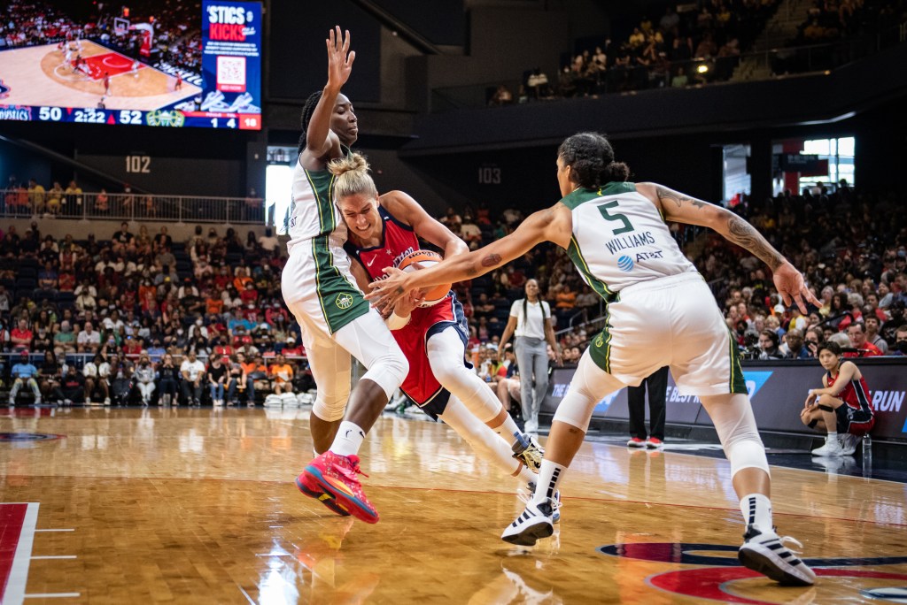 Mystics big Elena Delle Donne drives against Storm center Ezi Magbegor (13). Storm off-ball guard Gabby Williams (5) reaches out towards the ball.