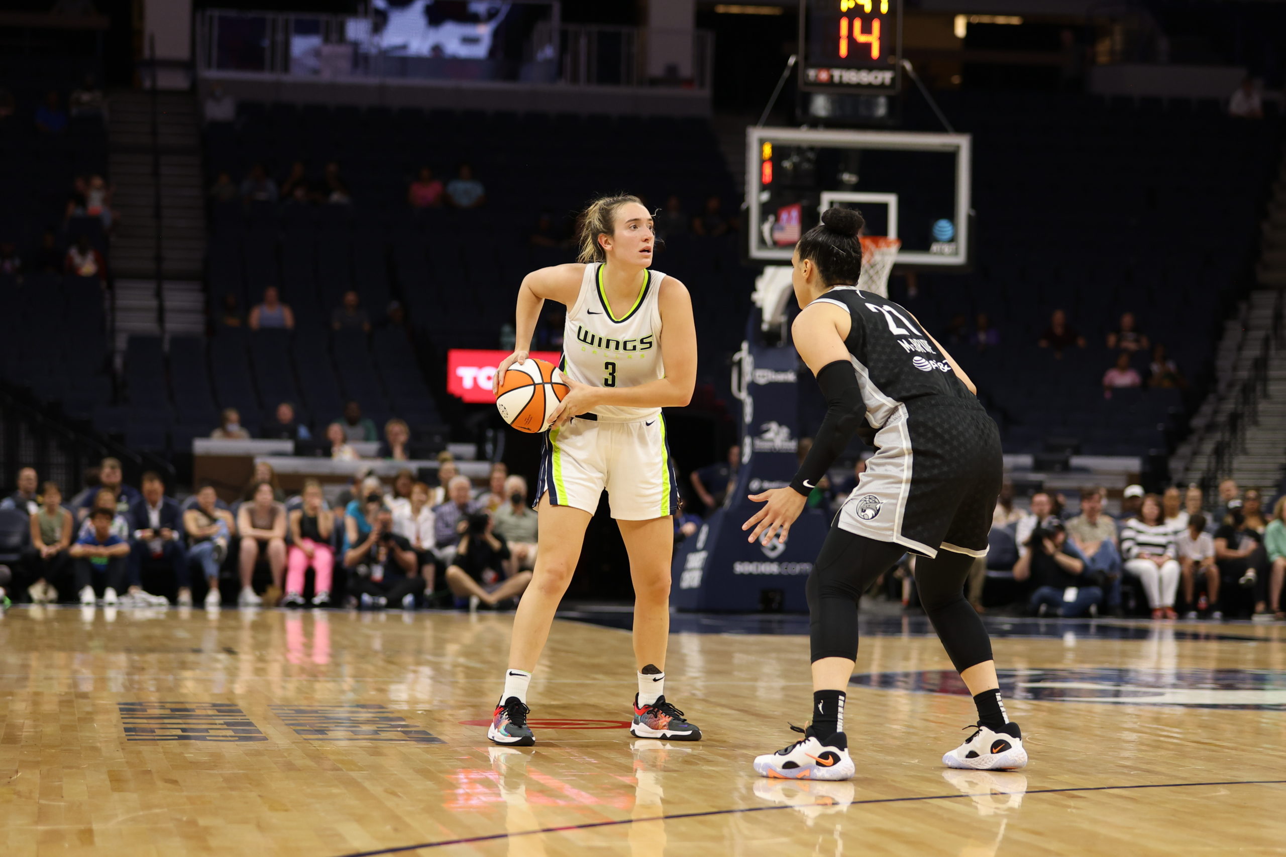 Dallas Wings wing Marina Mabrey stands above the slot in a triple-threat stance, as Minnesota Lynx off-ball guard Kayla McBride stands a foot in front of her, in a slight crouch to defend