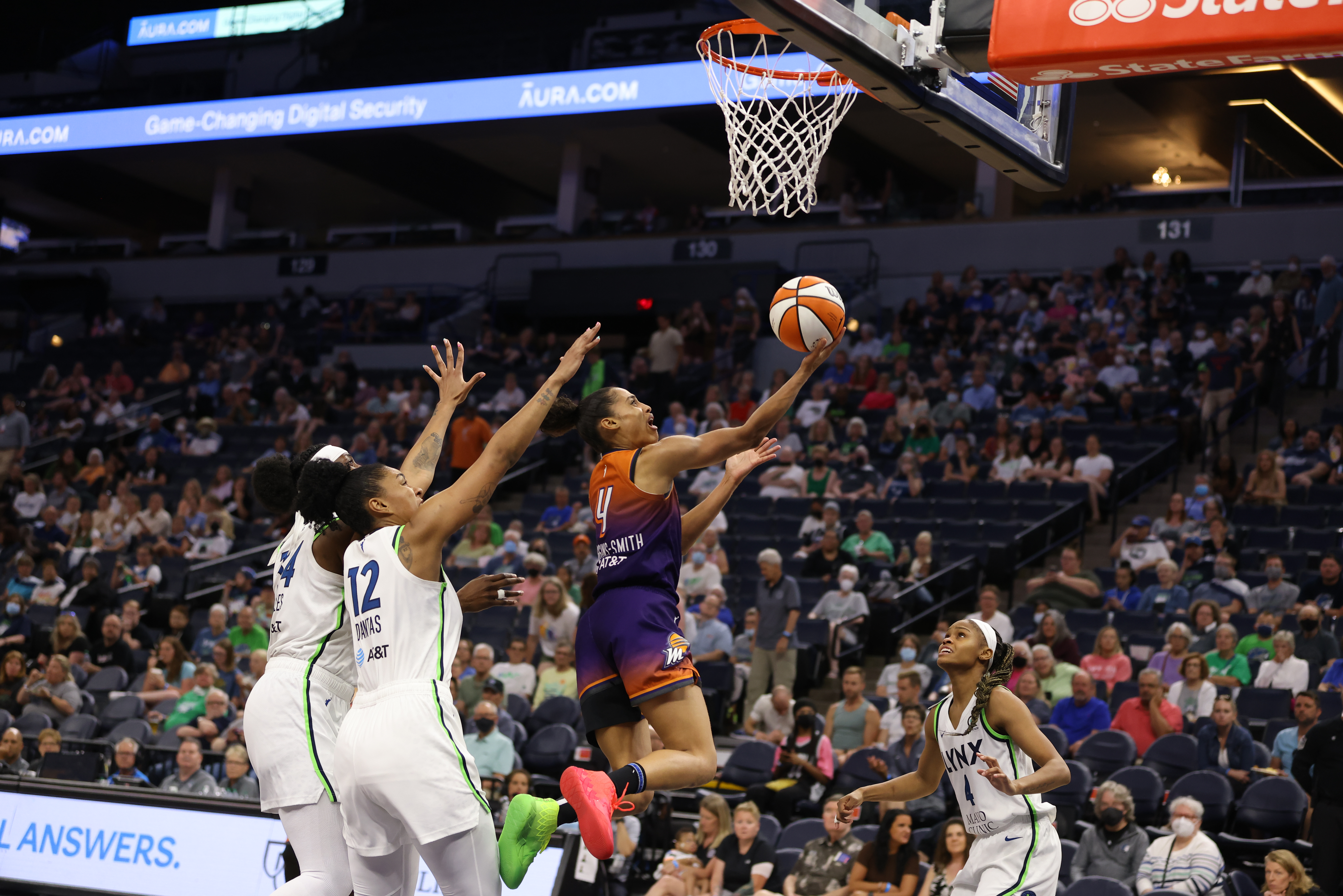 Phoenix Mercury combo guard Skylar Diggins-Smith, mid-air, shoots a reverse layup, while Minnesota big Damiris Dantas and center Sylvia Fowles stand behind her with their arms outstretched in an attempt to block the shot, and Lynx point guard Moriah Jefferson stands in front of Diggins-Smith looking up and watching